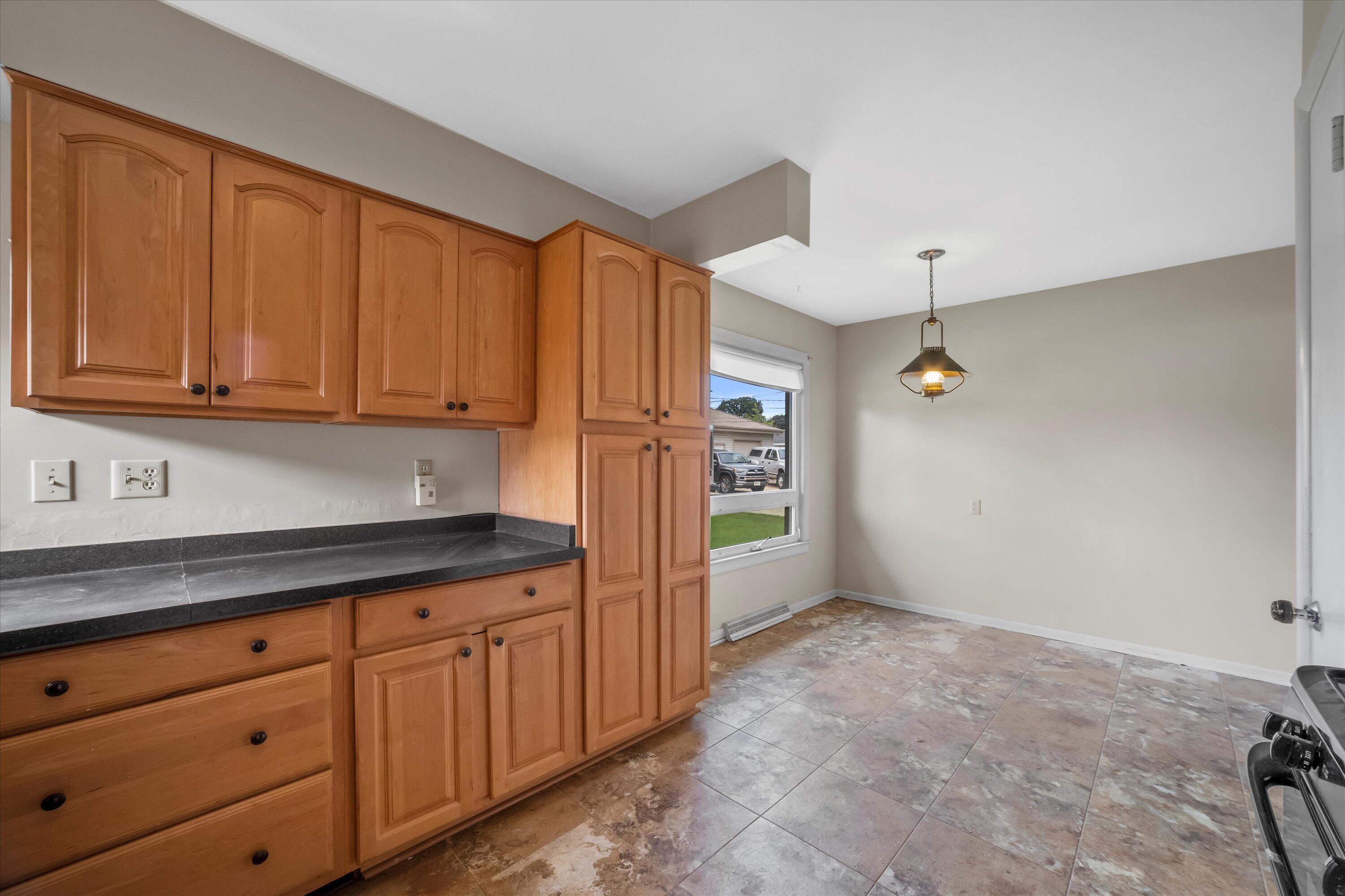 Vacant kitchen with honey-colored cabinets, dark countertops, and mottled tile flooring.