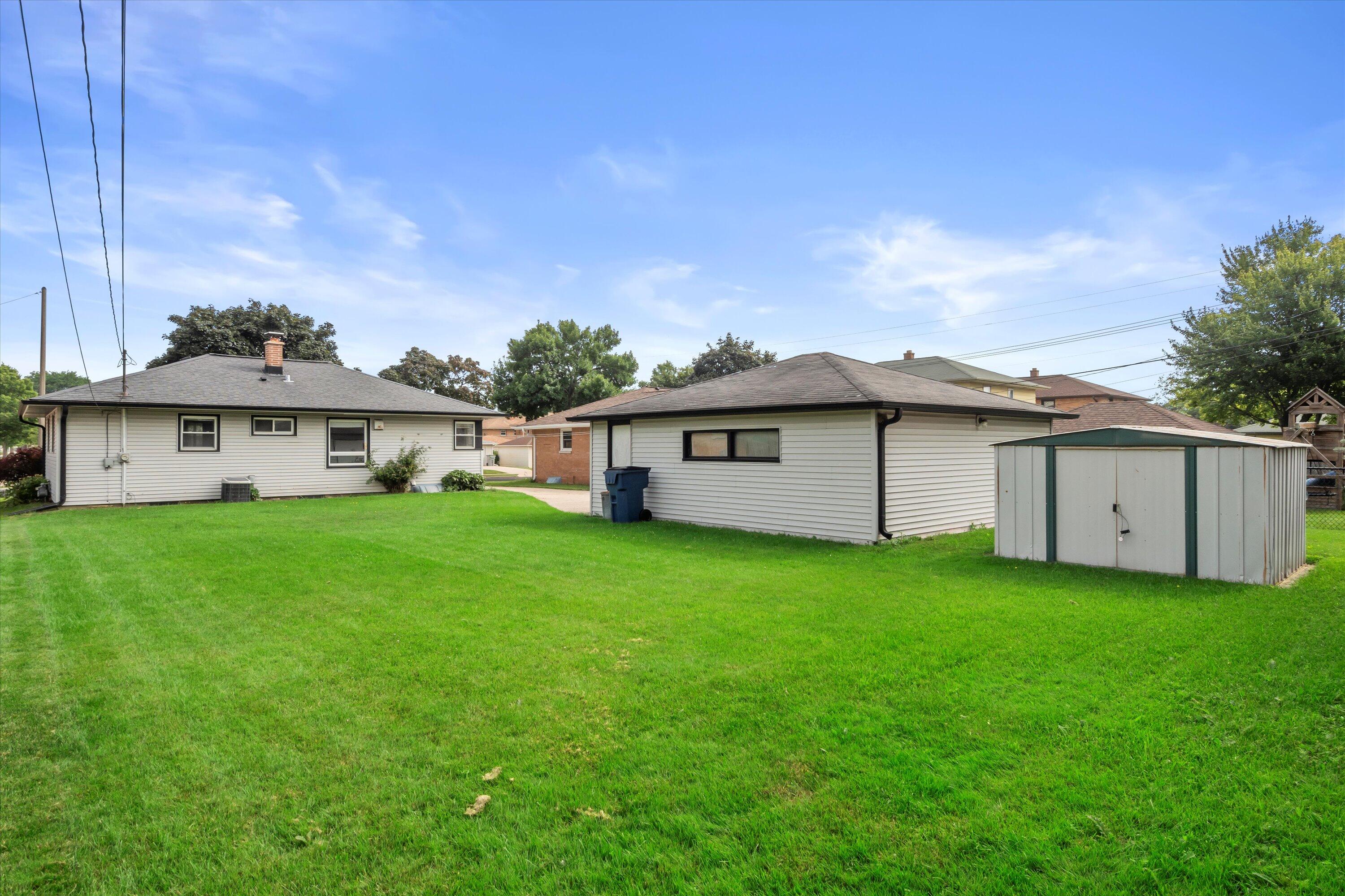 Rear of a single-story home with a broad lawn, detached garage, and storage shed.