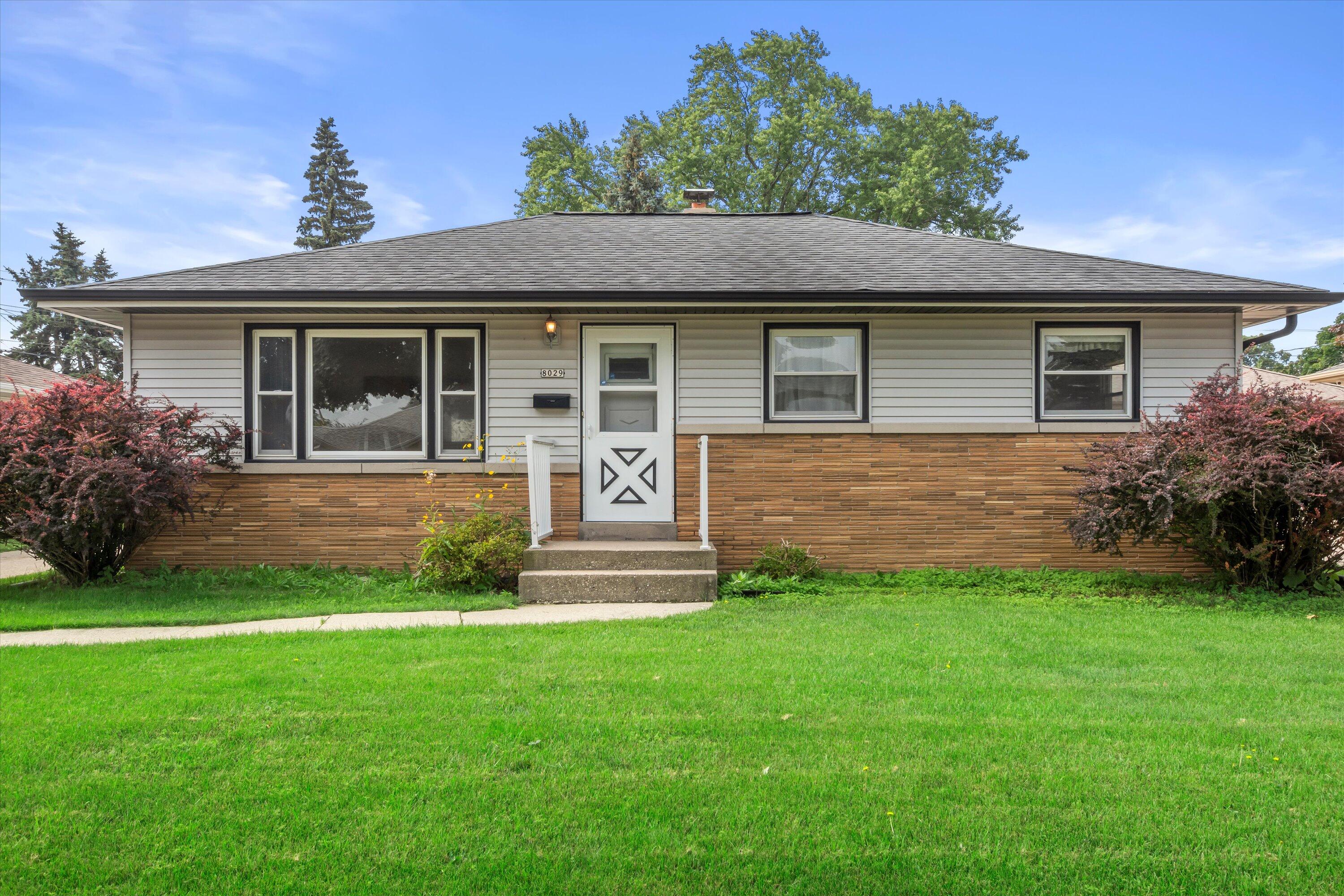 Single-story ranch home with a brick lower facade, white entry door, and broad green lawn.