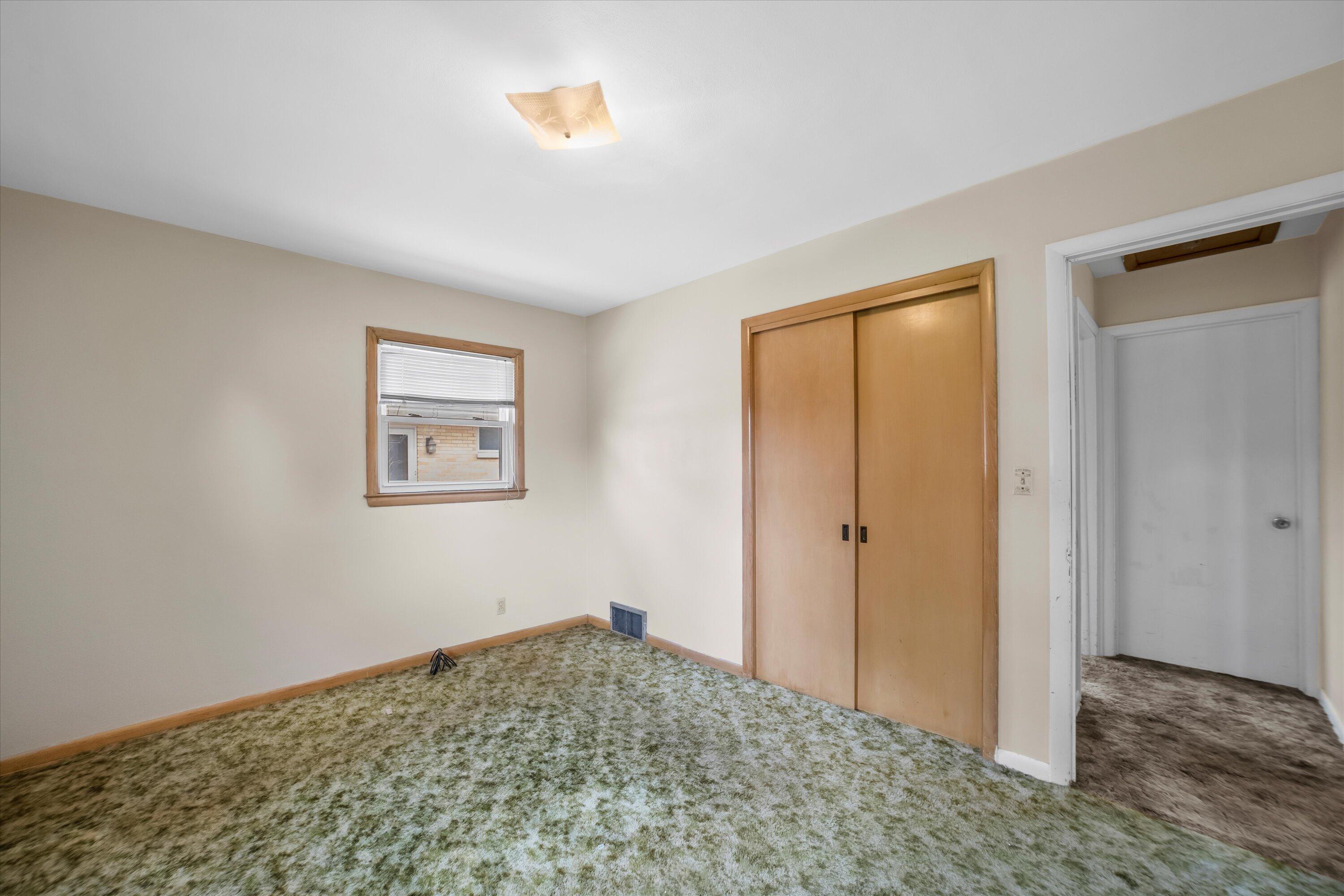 Empty bedroom with green patterned carpet, a small window, and wooden sliding closet doors.