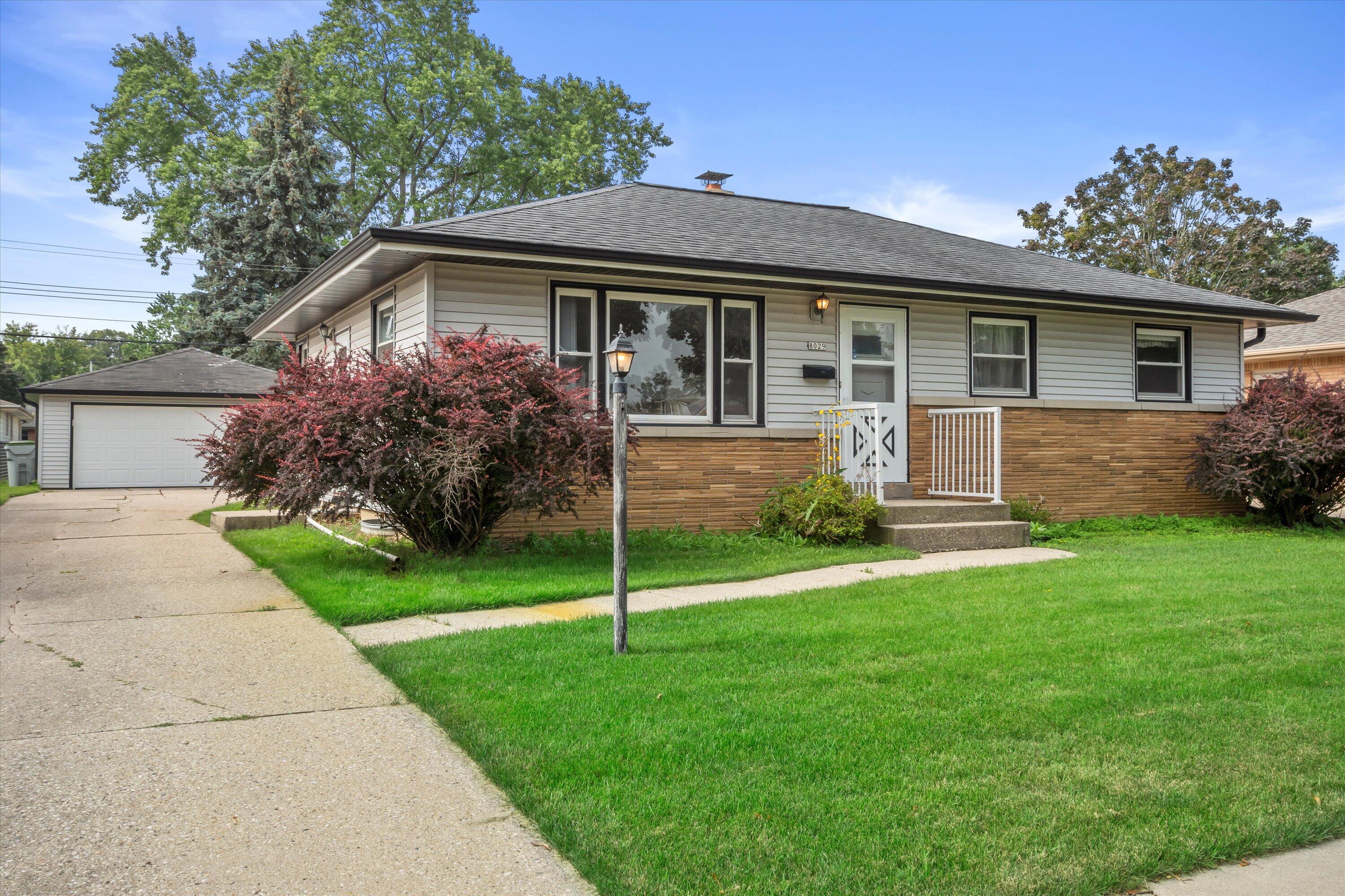 Single-story house with a brick lower facade, front stoop, landscaped lawn, and detached garage.