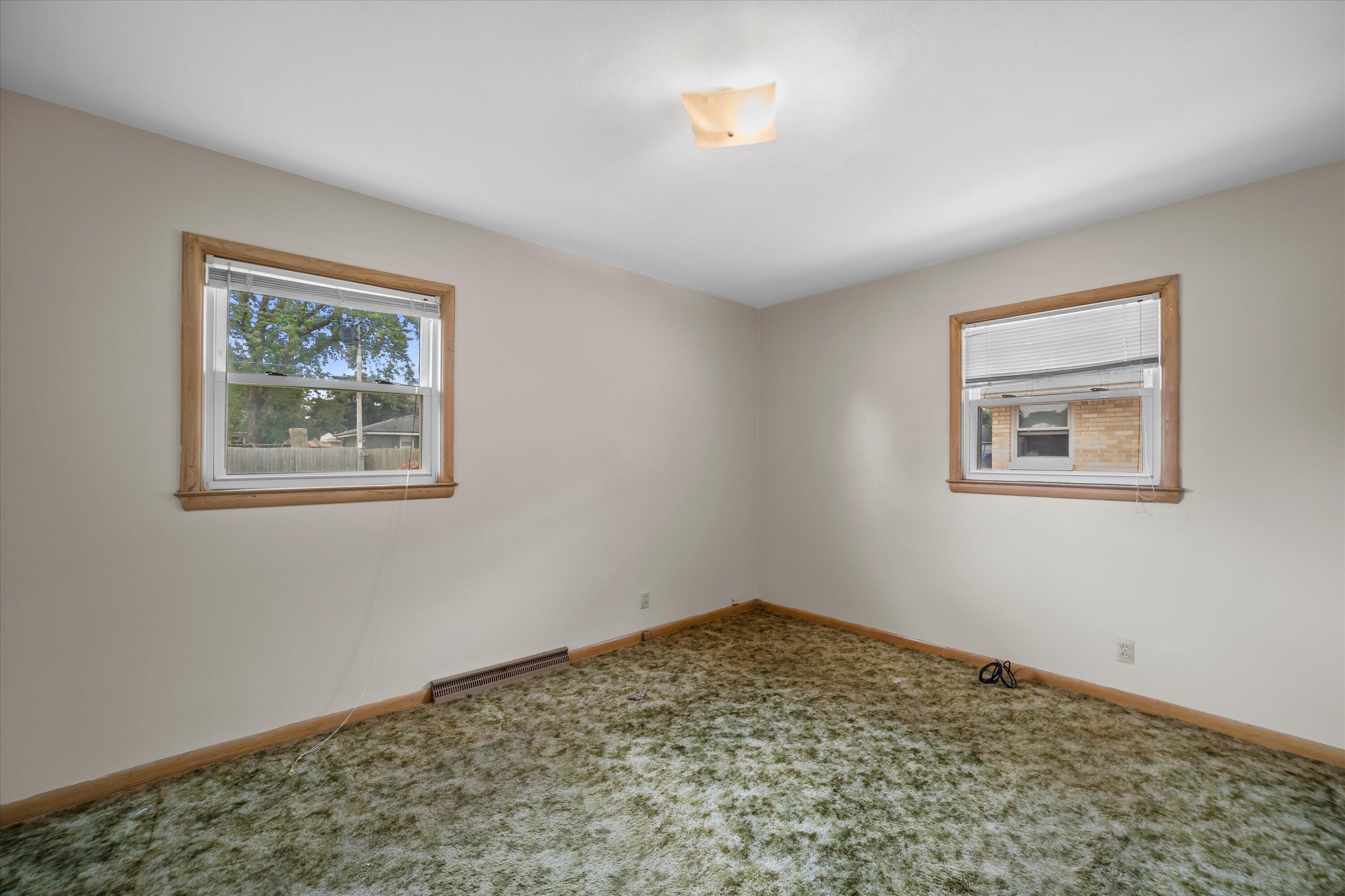 Empty bedroom with two wood-trimmed windows and mottled carpet.