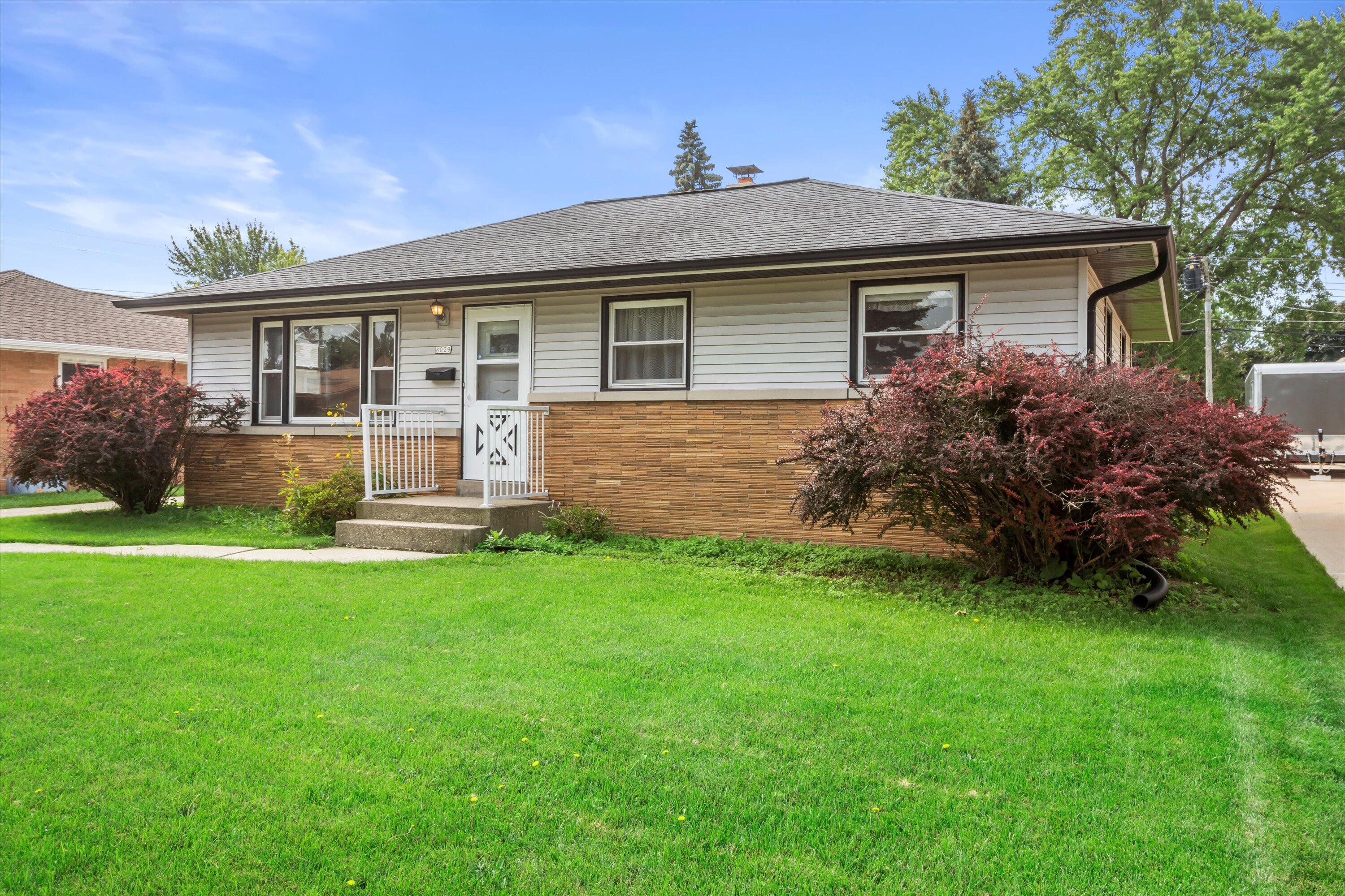 Single-story house with a brick lower facade, small railed entrance, and broad green lawn.