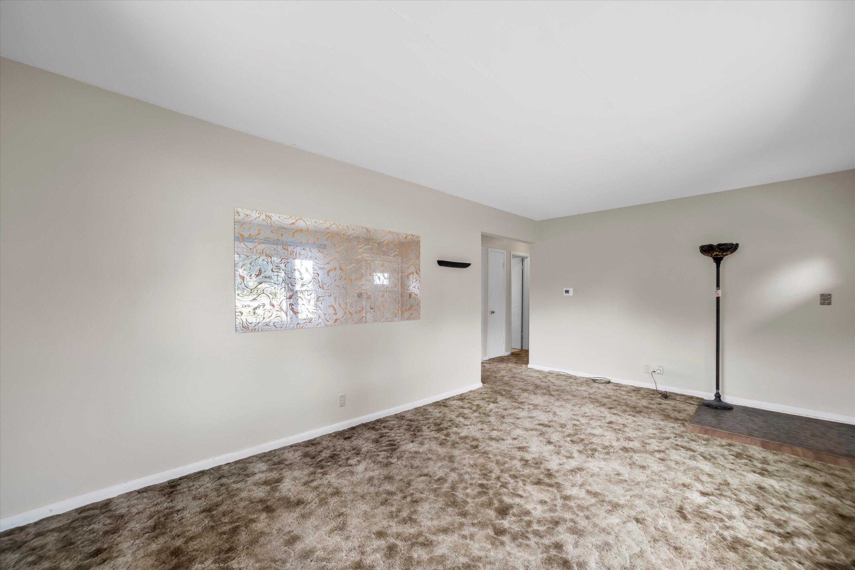 Unfurnished living room with plush brown carpet, decorative wall art, and a tall floor lamp.