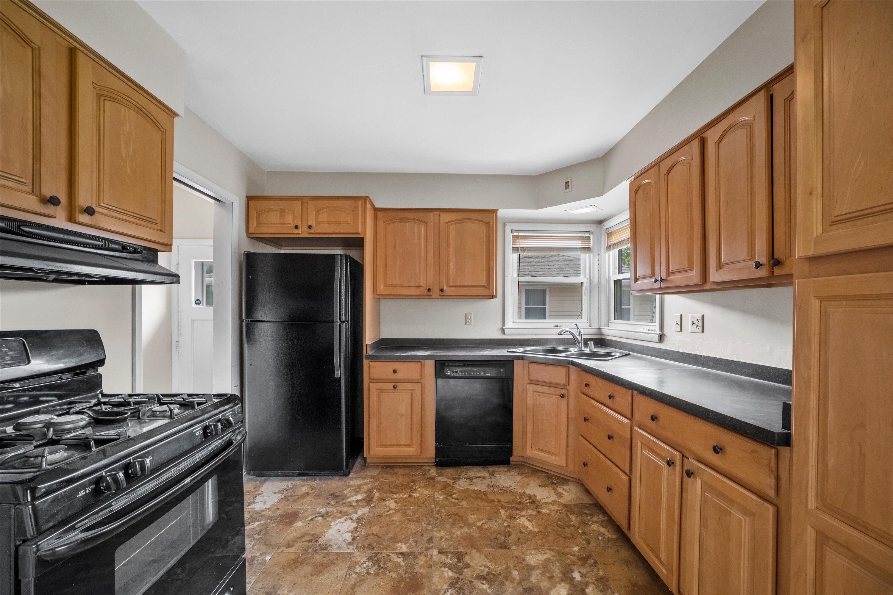 Kitchen with honey-colored wood cabinets, black appliances, a corner sink, and patterned tile flooring.