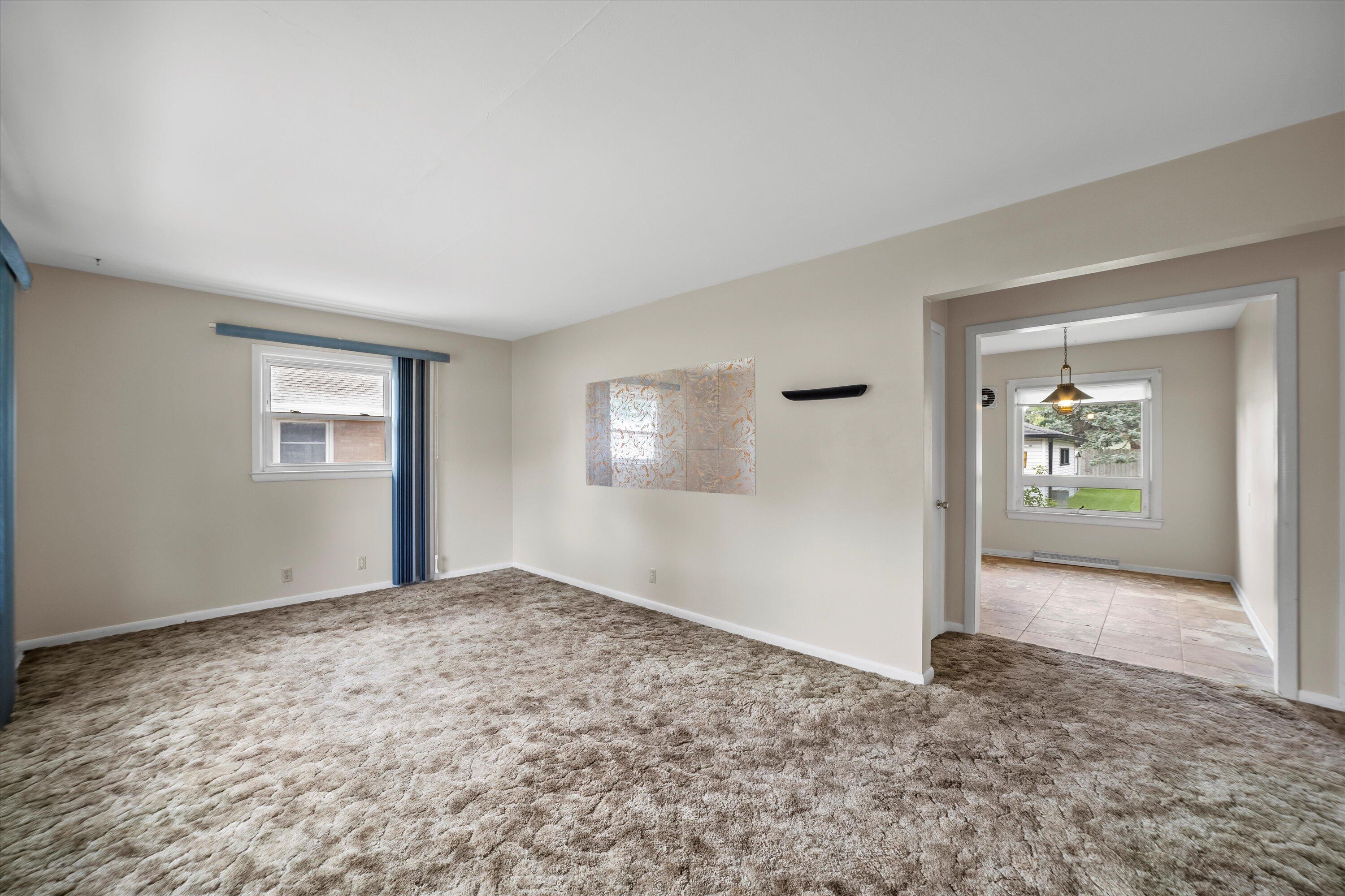 Mostly empty living room with plush patterned carpet and a wide doorway to a tiled room.