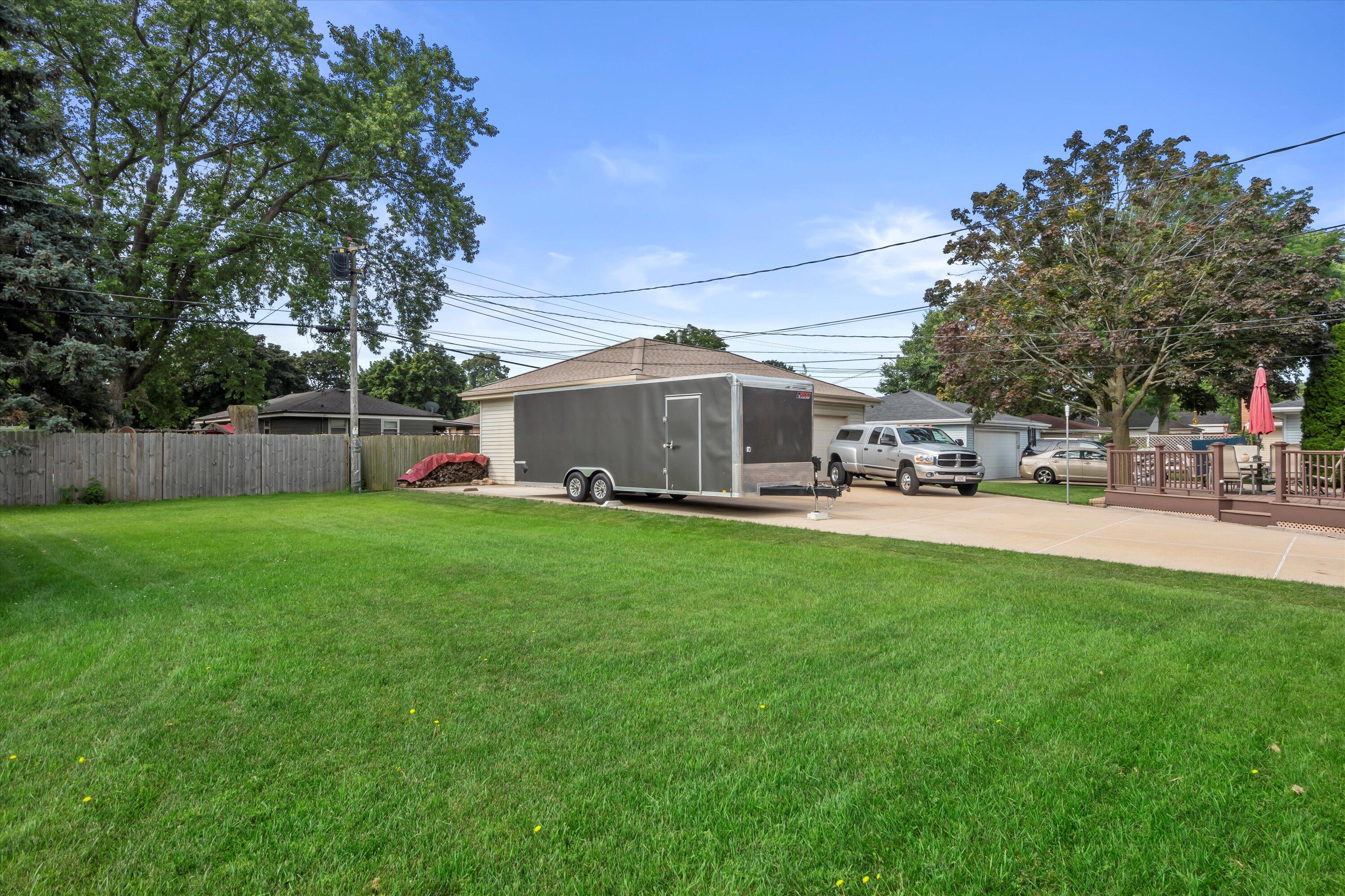 Backyard with a broad lawn, driveway, detached garage, and raised deck.