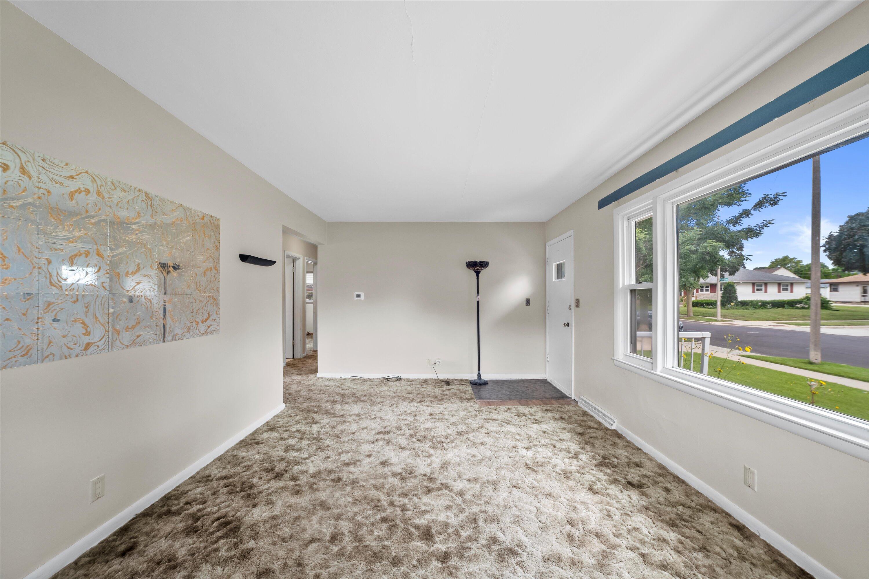 Living room with plush carpet, patterned wall art, and a large street-facing picture window.