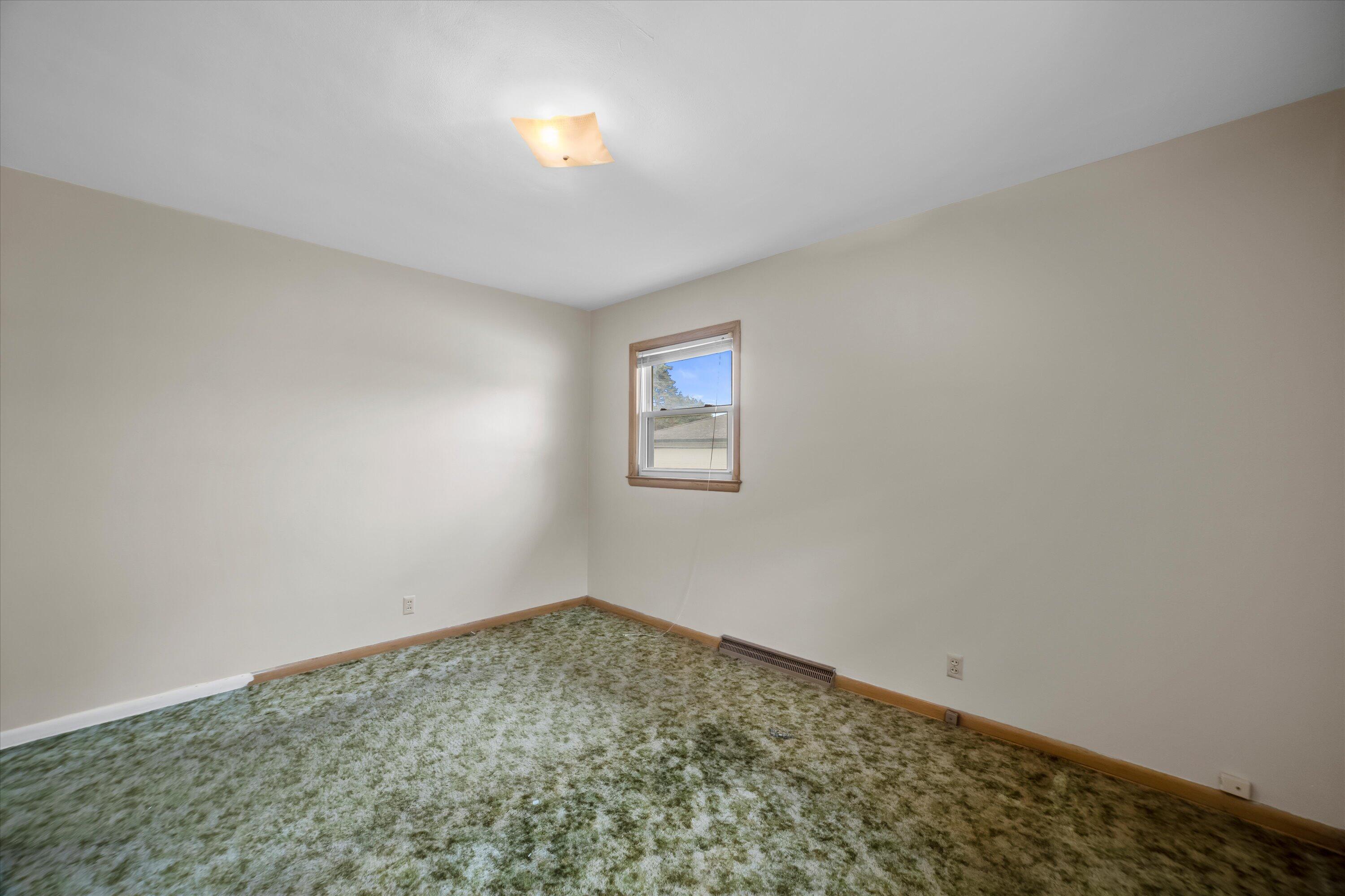 Empty bedroom with mottled green carpet, wood trim, and one window.