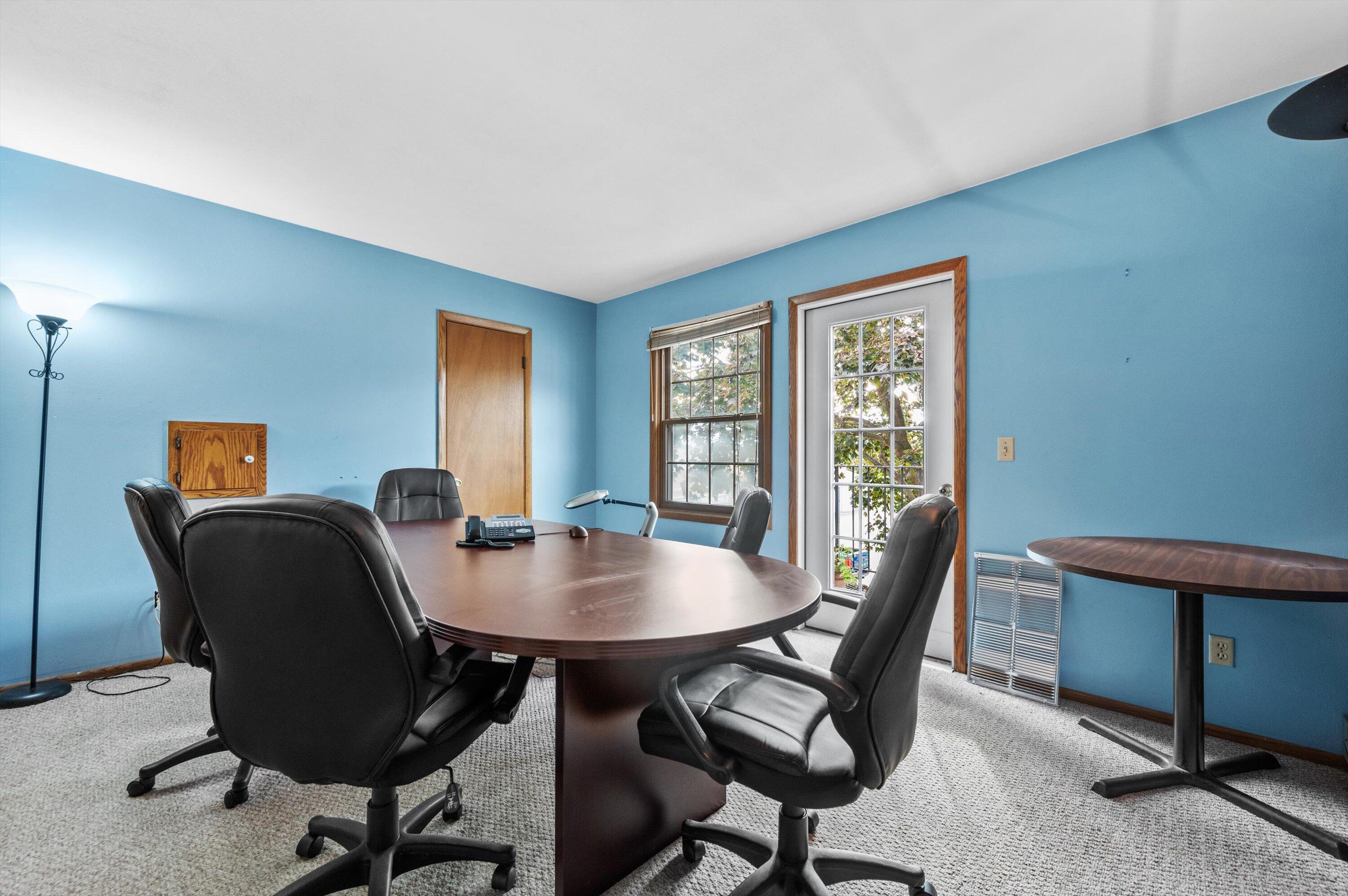Furnished office with blue walls, an oval conference table, black chairs, and a glass door.