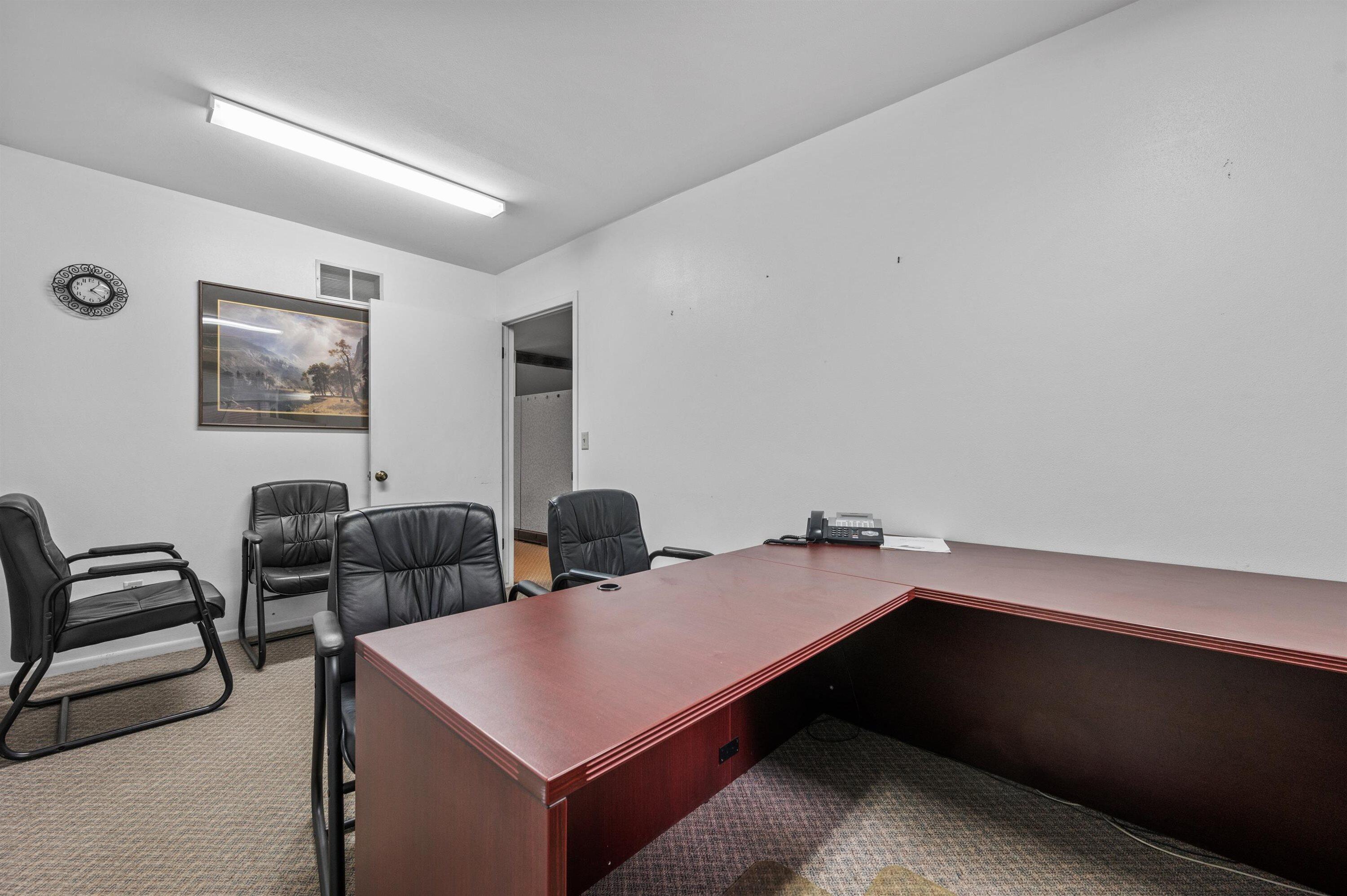 Office with a large L-shaped wood desk and black leather chairs.