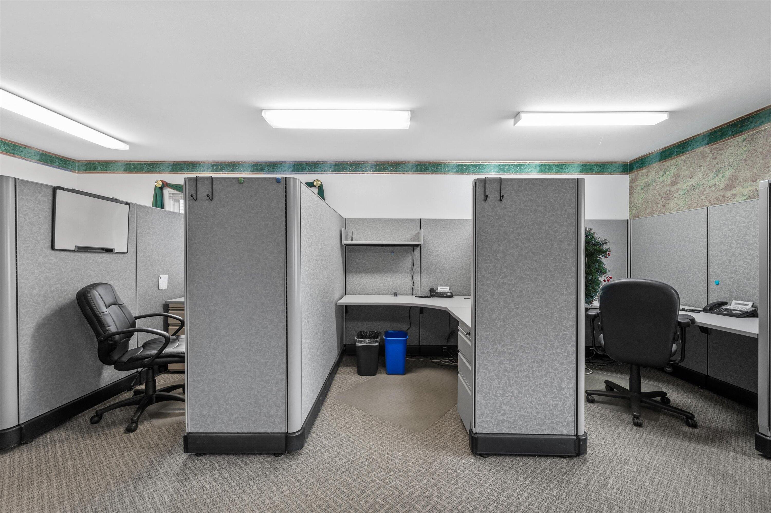 Office interior with gray cubicles, desks, and black office chairs.