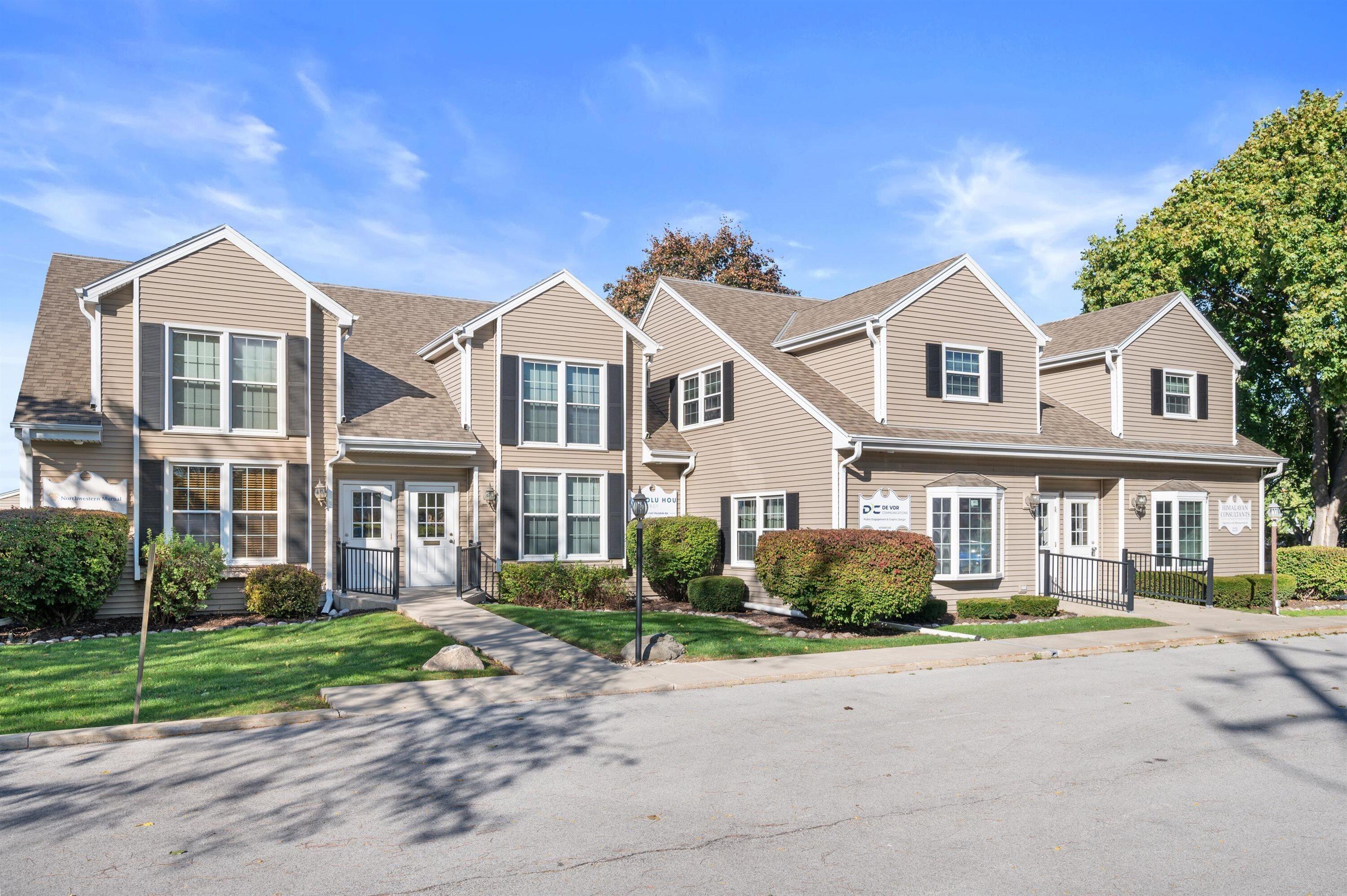 Beige commercial building with multiple gables, black shutters, landscaped shrubs, and several sidewalk entrances.