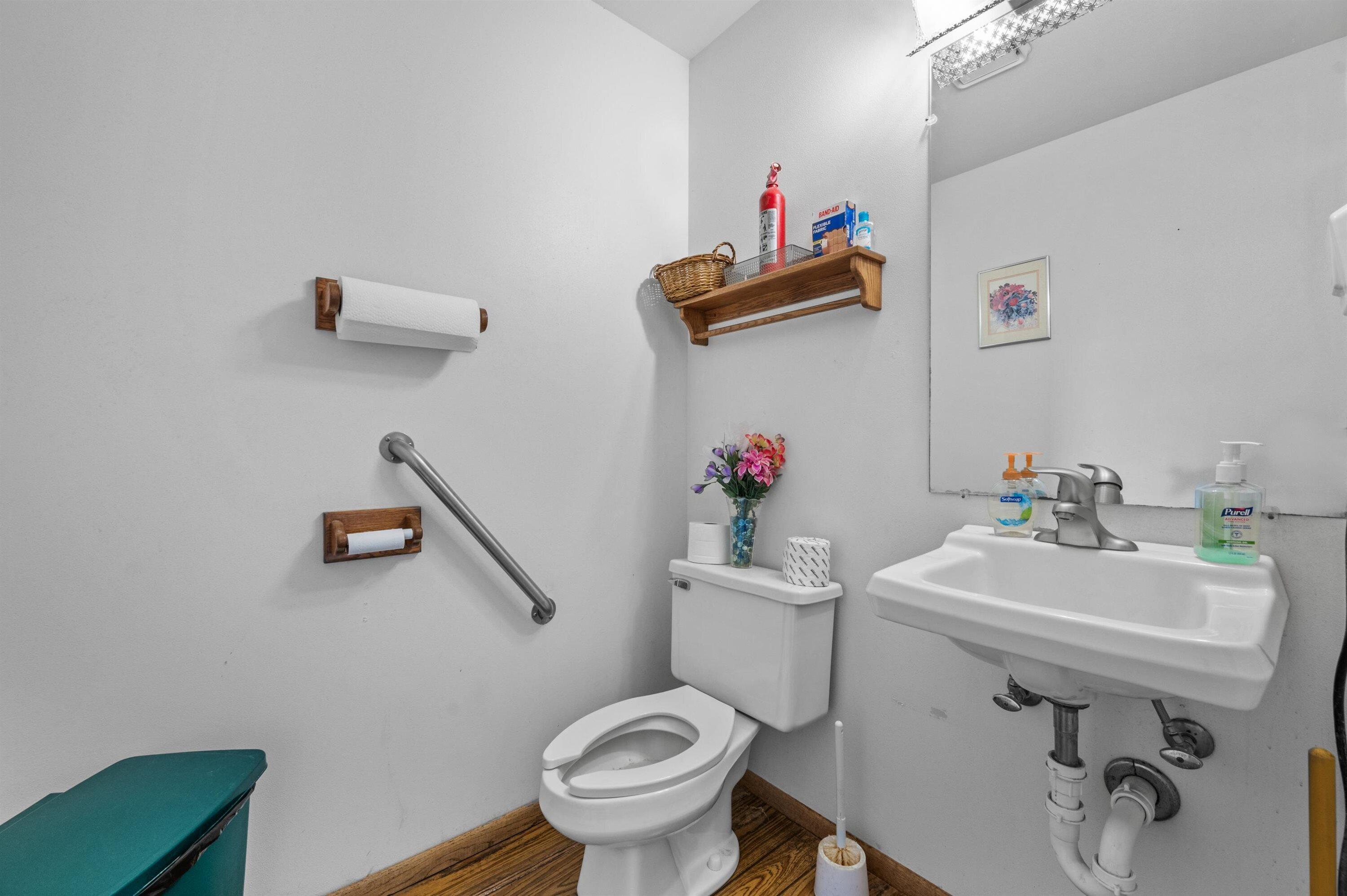 Bathroom with toilet, wall-mounted sink, metal grab bar, and wood flooring.