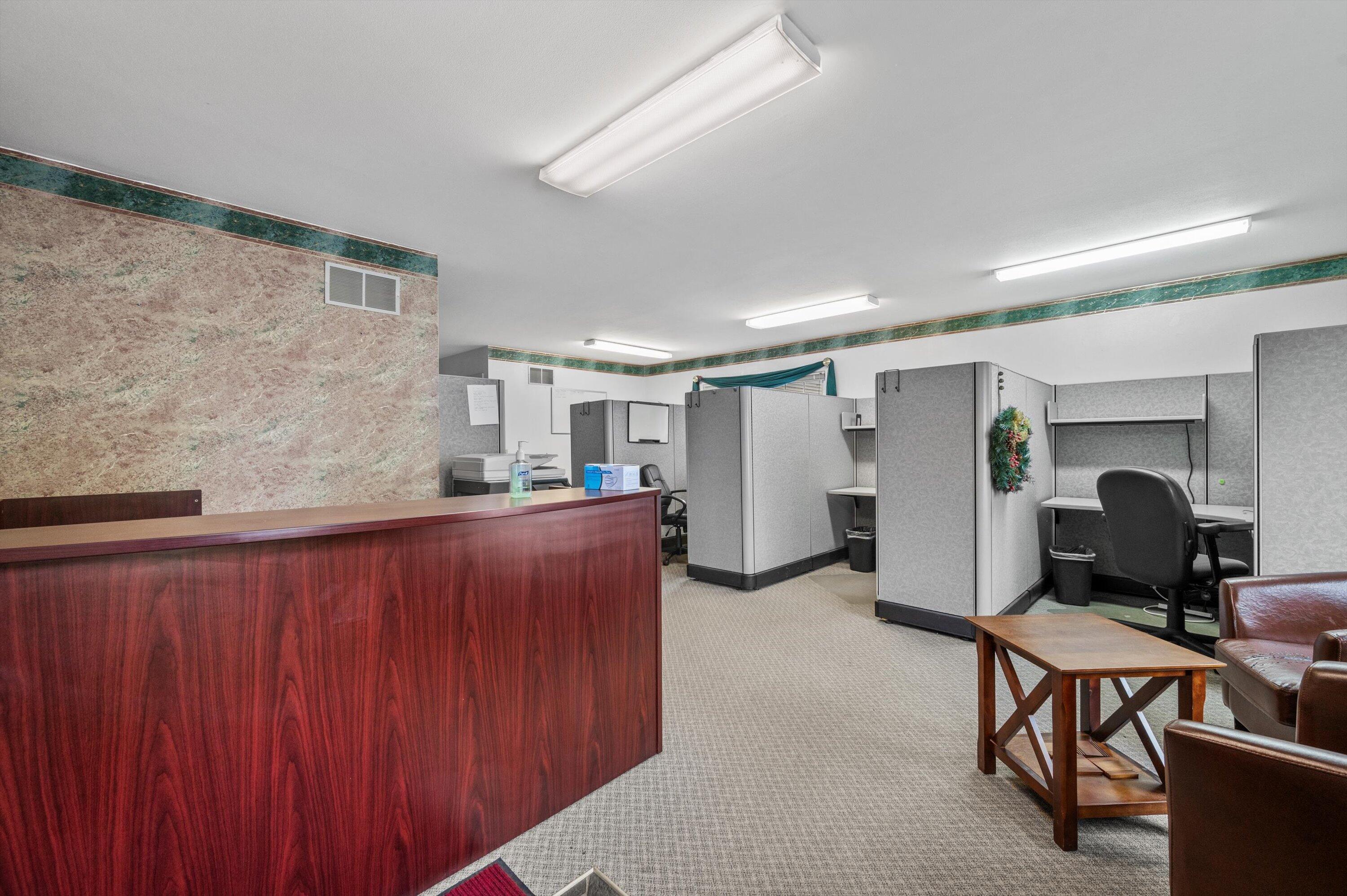 Office reception area with a wood counter and rows of gray cubicles.