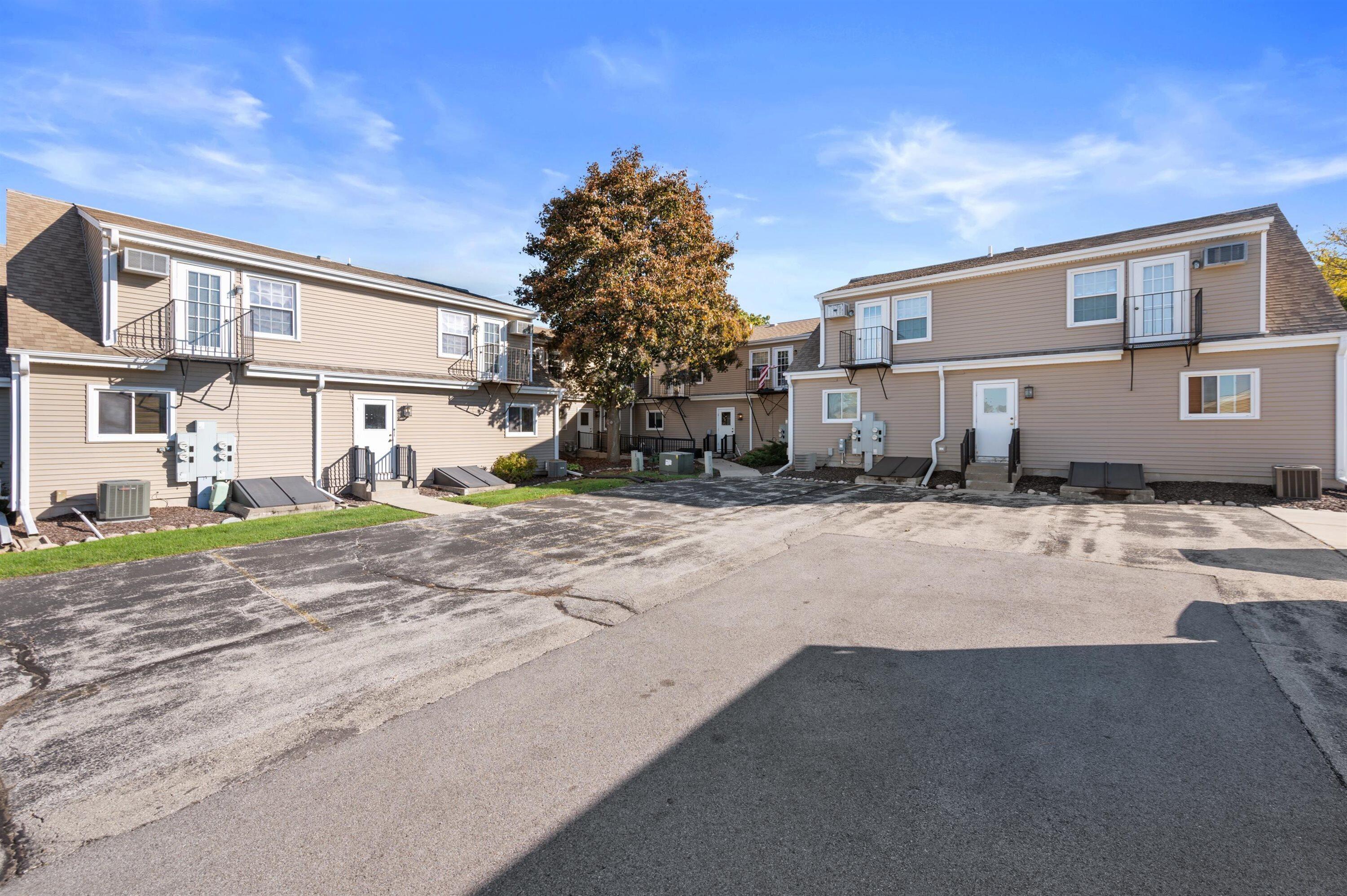Multi-unit residential buildings with tan siding and balconies around a paved parking area.