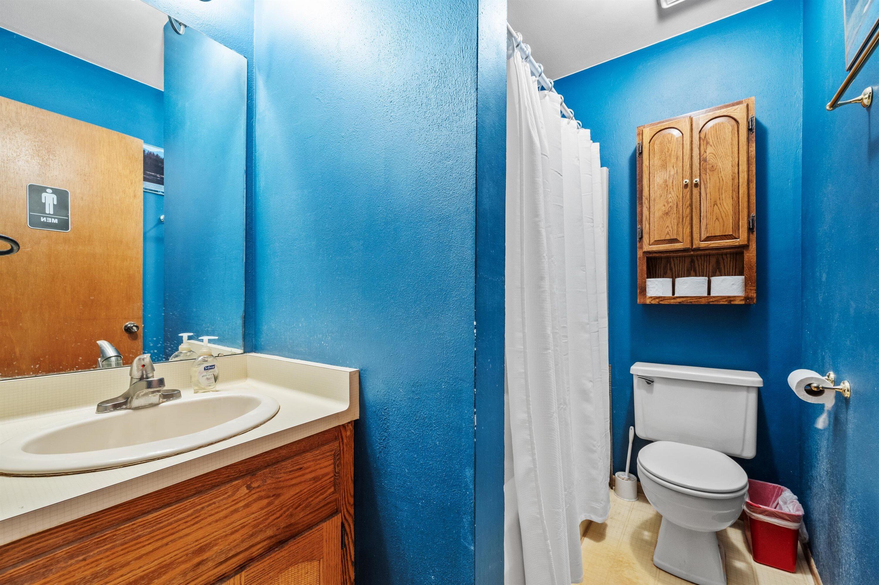 Bathroom with vivid blue walls, a white shower curtain, and a wooden cabinet above the toilet.