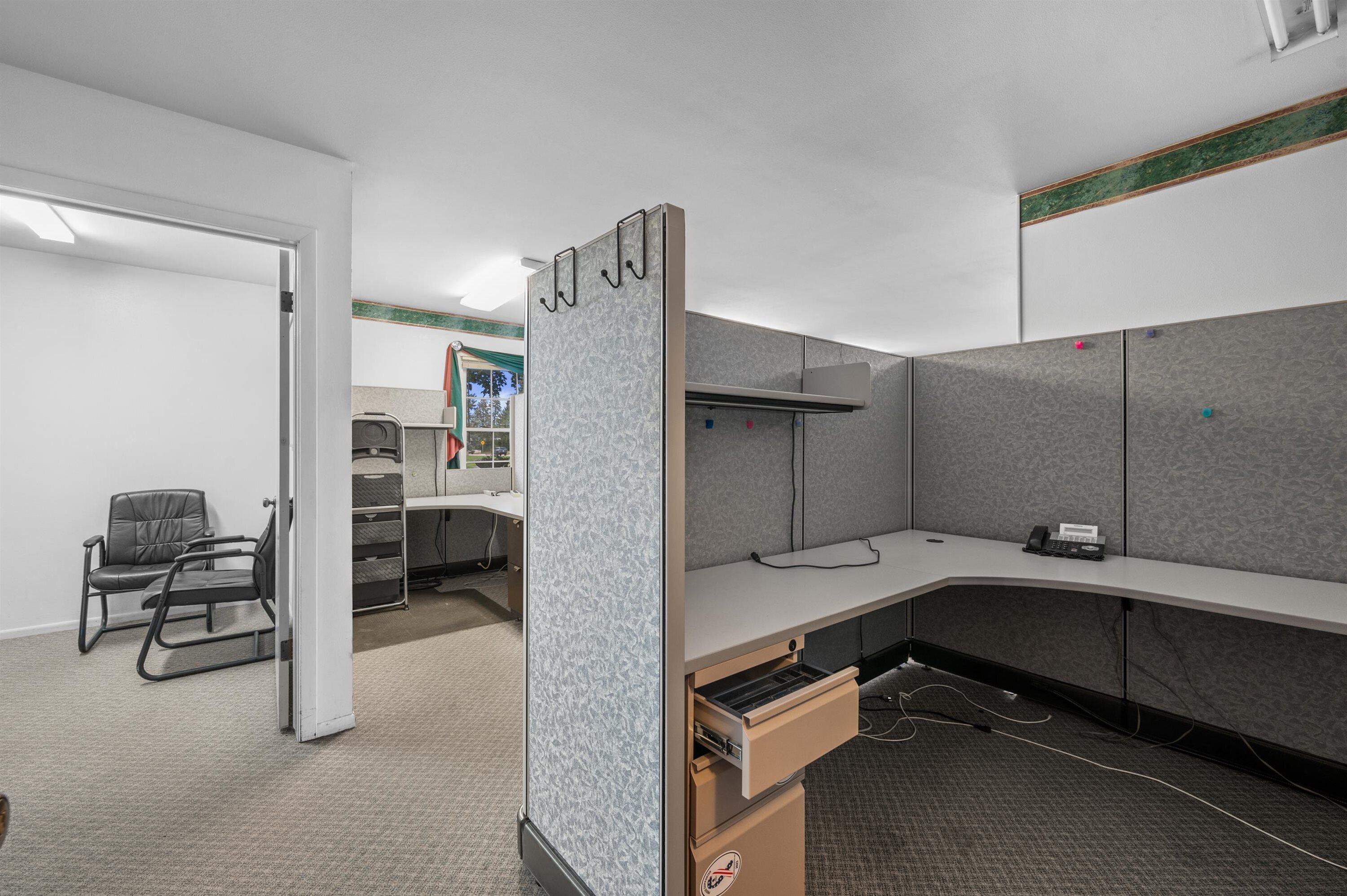 Office interior with gray cubicles, L-shaped desks, and a separate seating area.