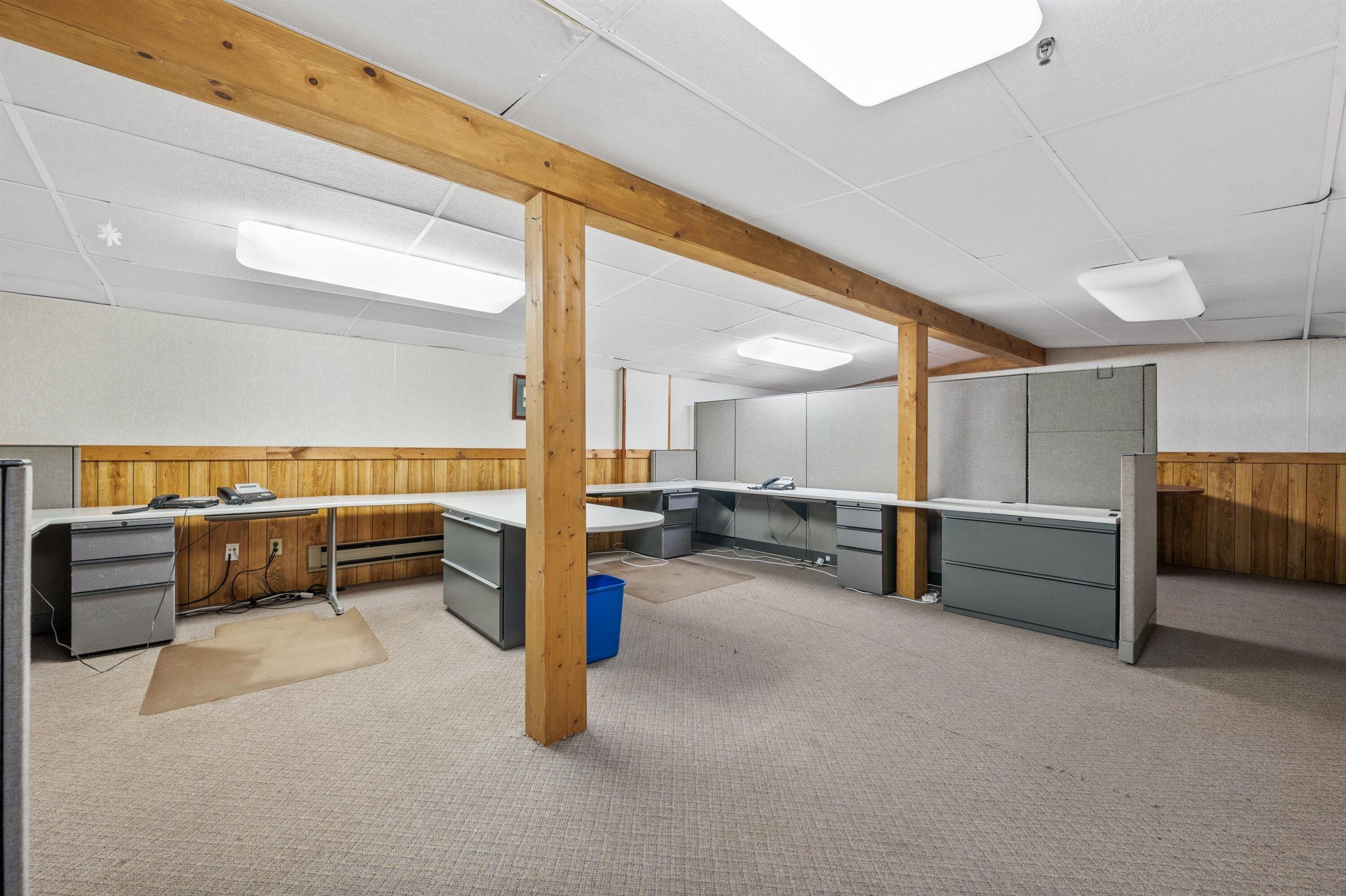 Office space with gray cubicles and desks beneath exposed timber beams.