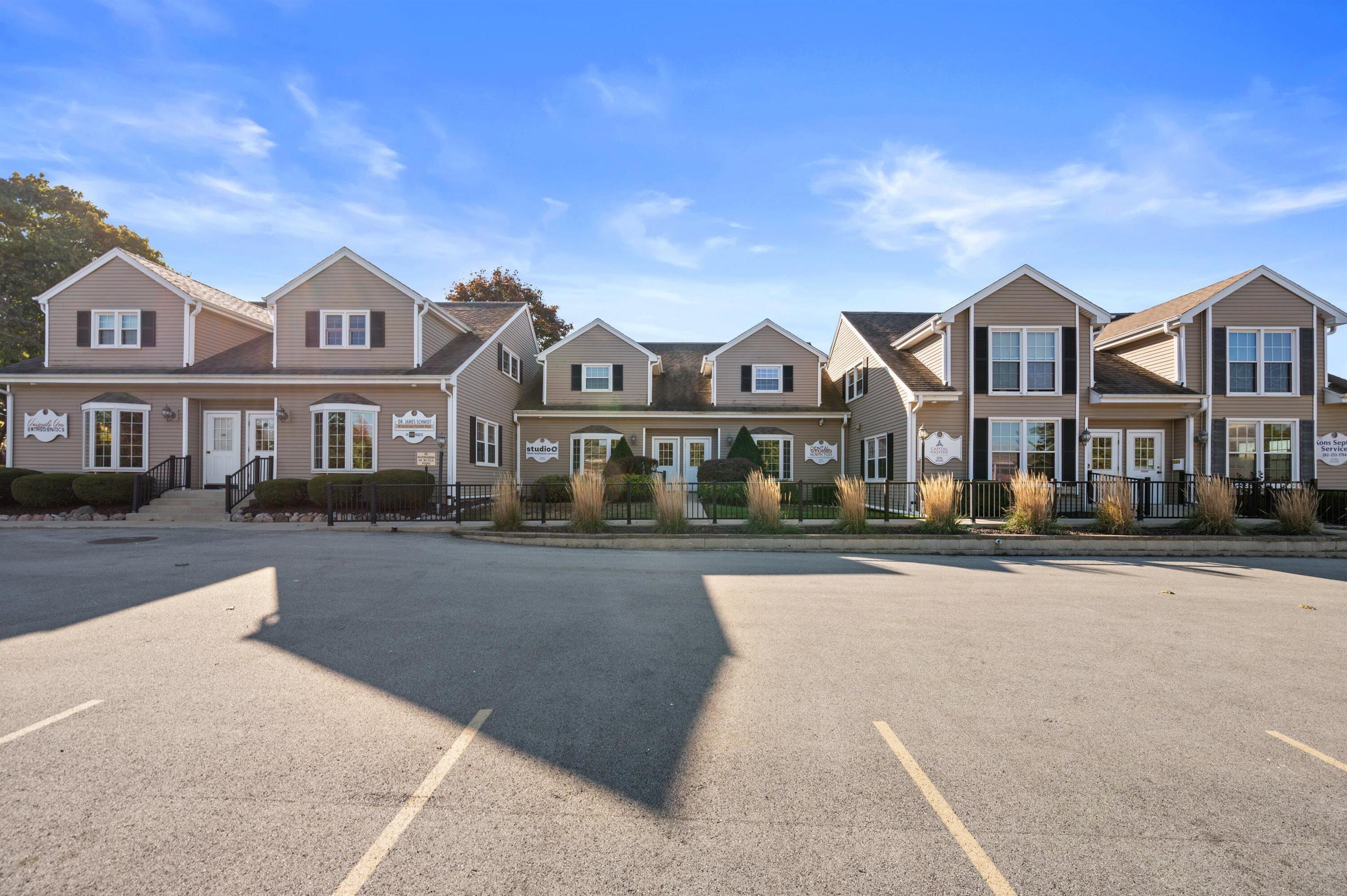 Connected tan commercial buildings with multiple entrances and a parking lot in front.