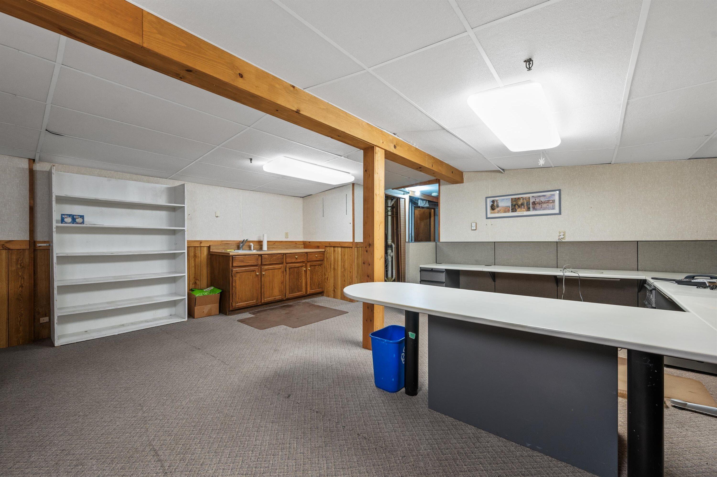 Office with gray cubicle desks, a large white worktable, and exposed timber beams.