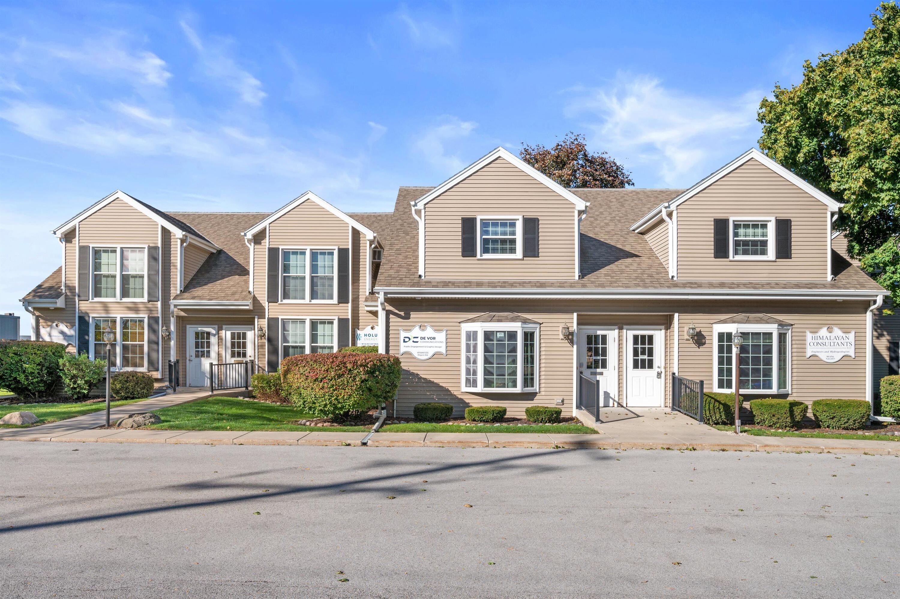 Two-story tan commercial building with gabled roof sections, white-trimmed windows, and landscaped frontage.