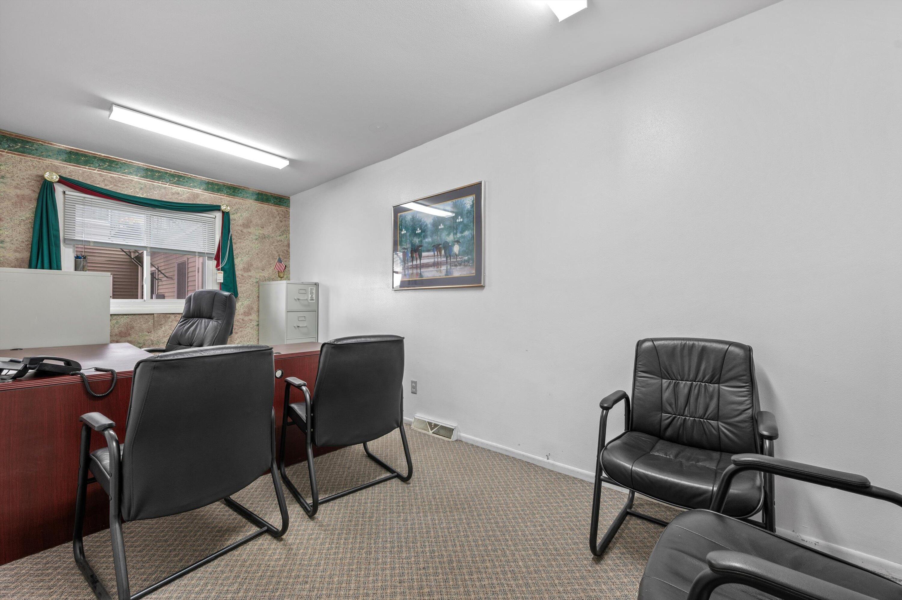 Office with a dark wood desk, black leather chairs, patterned carpet, and a window with blinds.