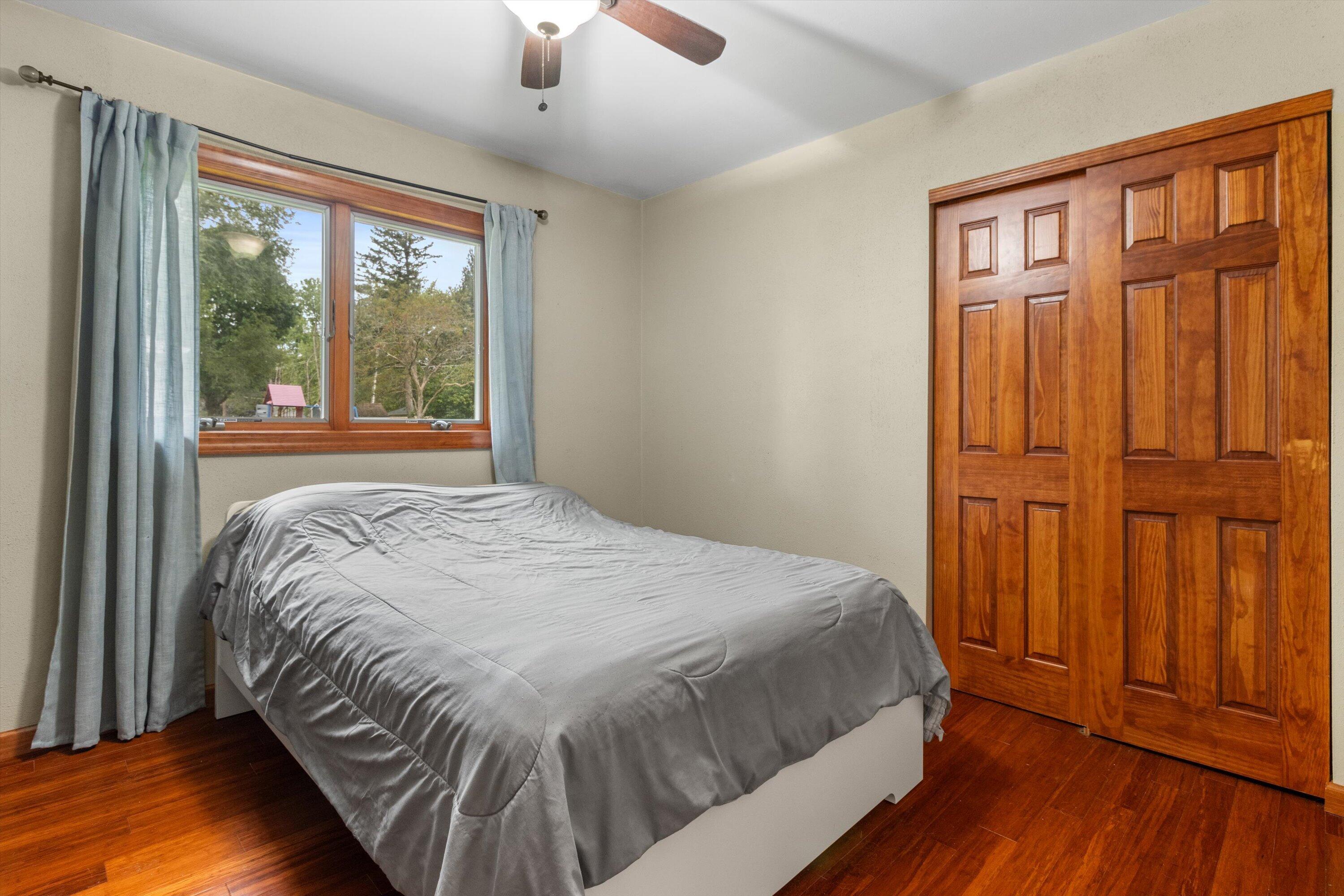 Bedroom with gray bedding, hardwood floors, blue curtains, and paneled wooden closet doors.