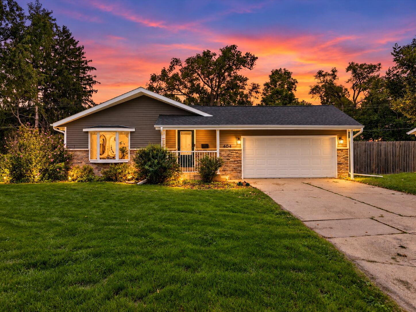 Single-story gray house with stone accents and a double garage beneath a colorful sunset.