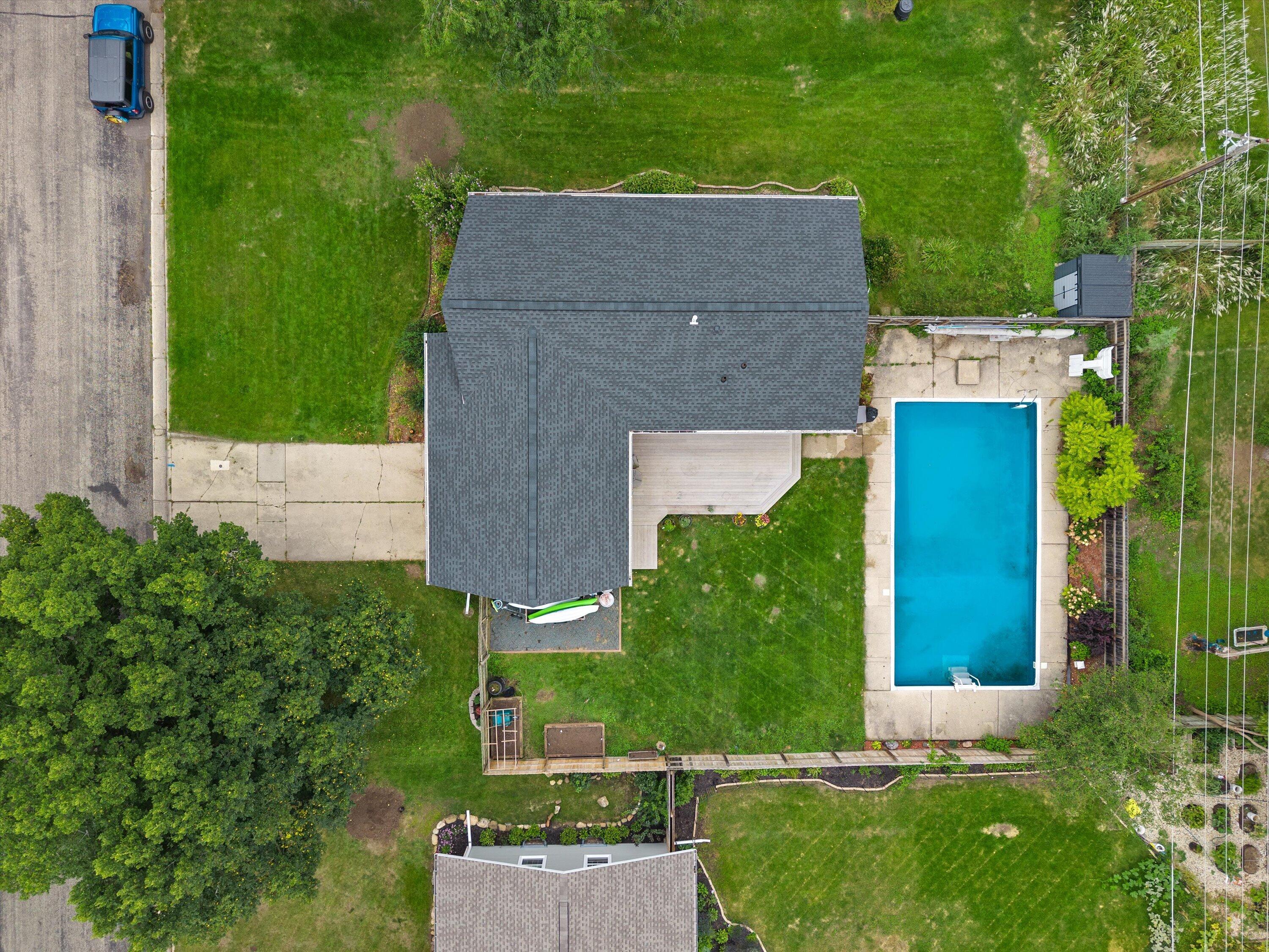 Aerial view of a house with a rectangular backyard pool, patio, and fenced lawn.
