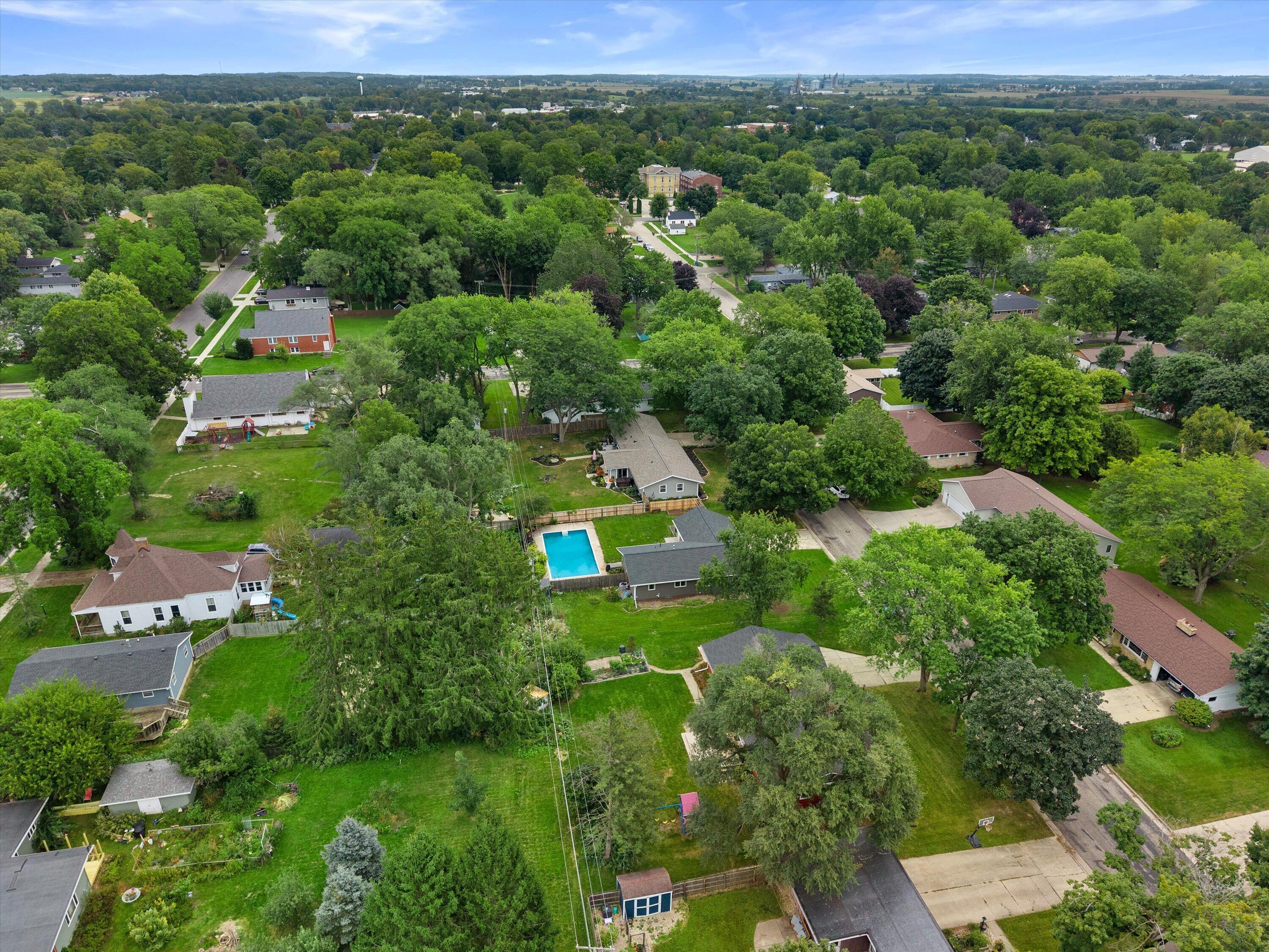 Aerial view of a tree-lined residential property with a backyard pool and surrounding homes.