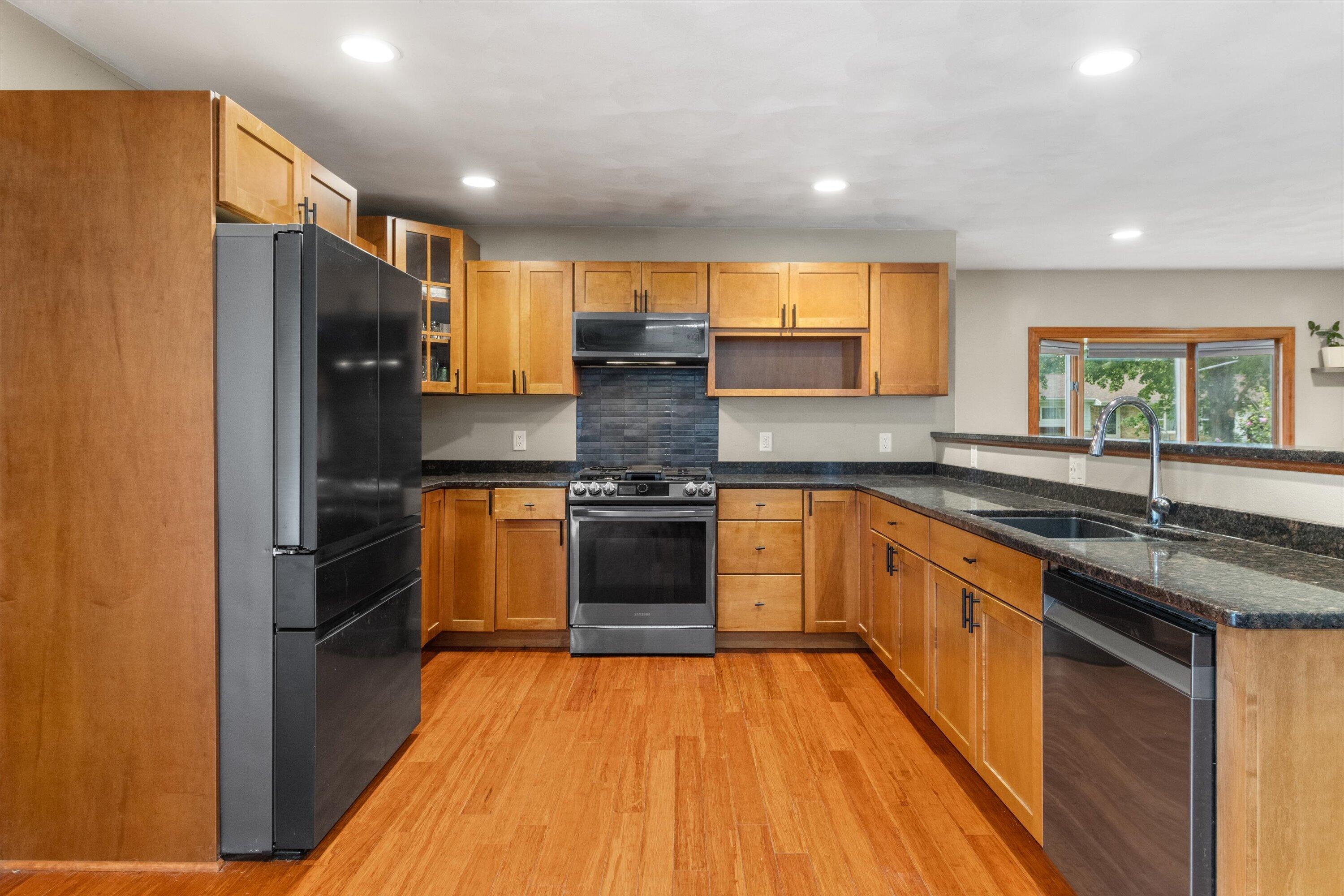 Kitchen with wood cabinets, dark countertops, stainless steel appliances, and a window above the sink.