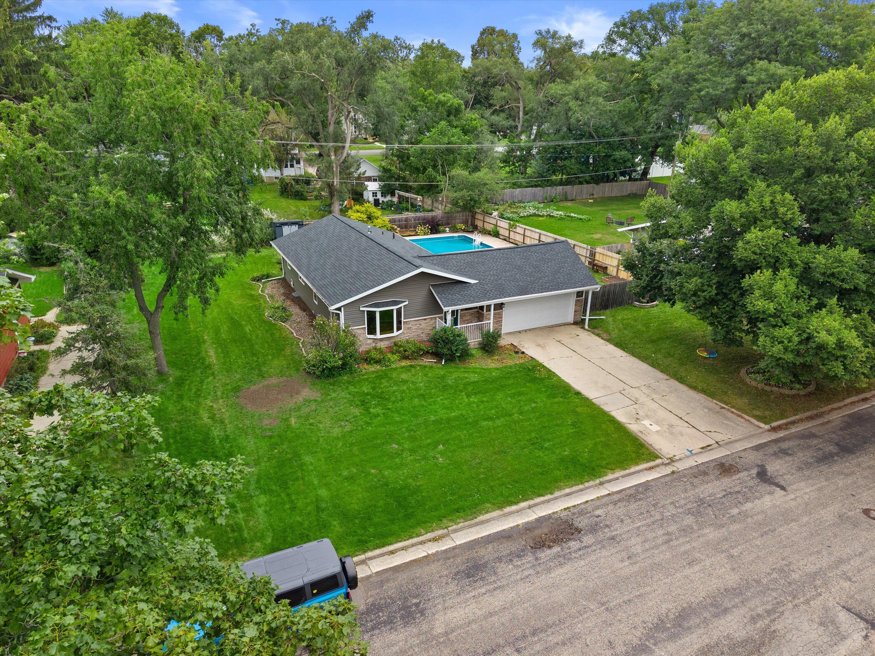 Aerial view of a single-story home with a fenced backyard pool and mature trees.