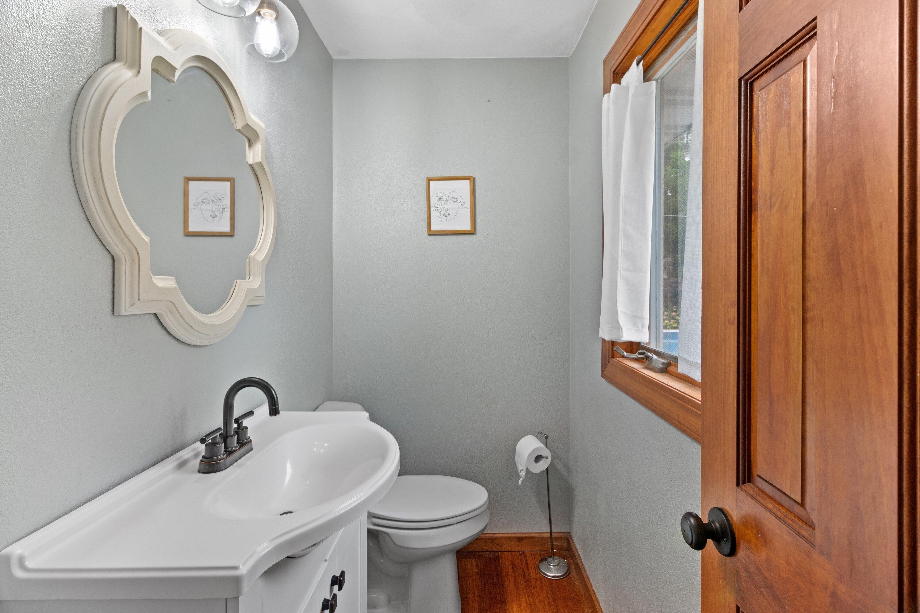 Bathroom with a white vanity, ornate mirror, toilet, and warm wood flooring and trim.