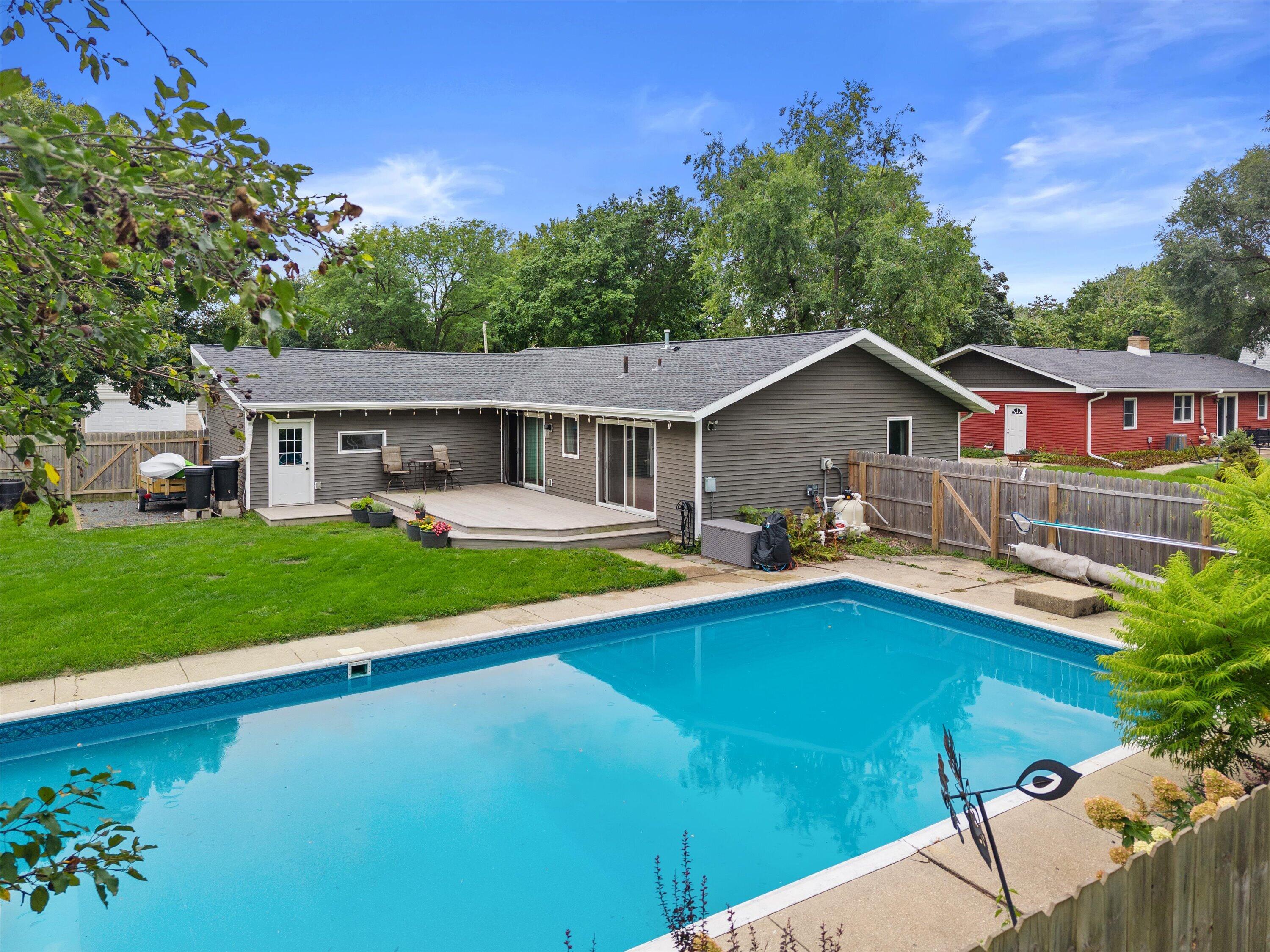 Home’s rear patio and fenced yard overlooking a large swimming pool.