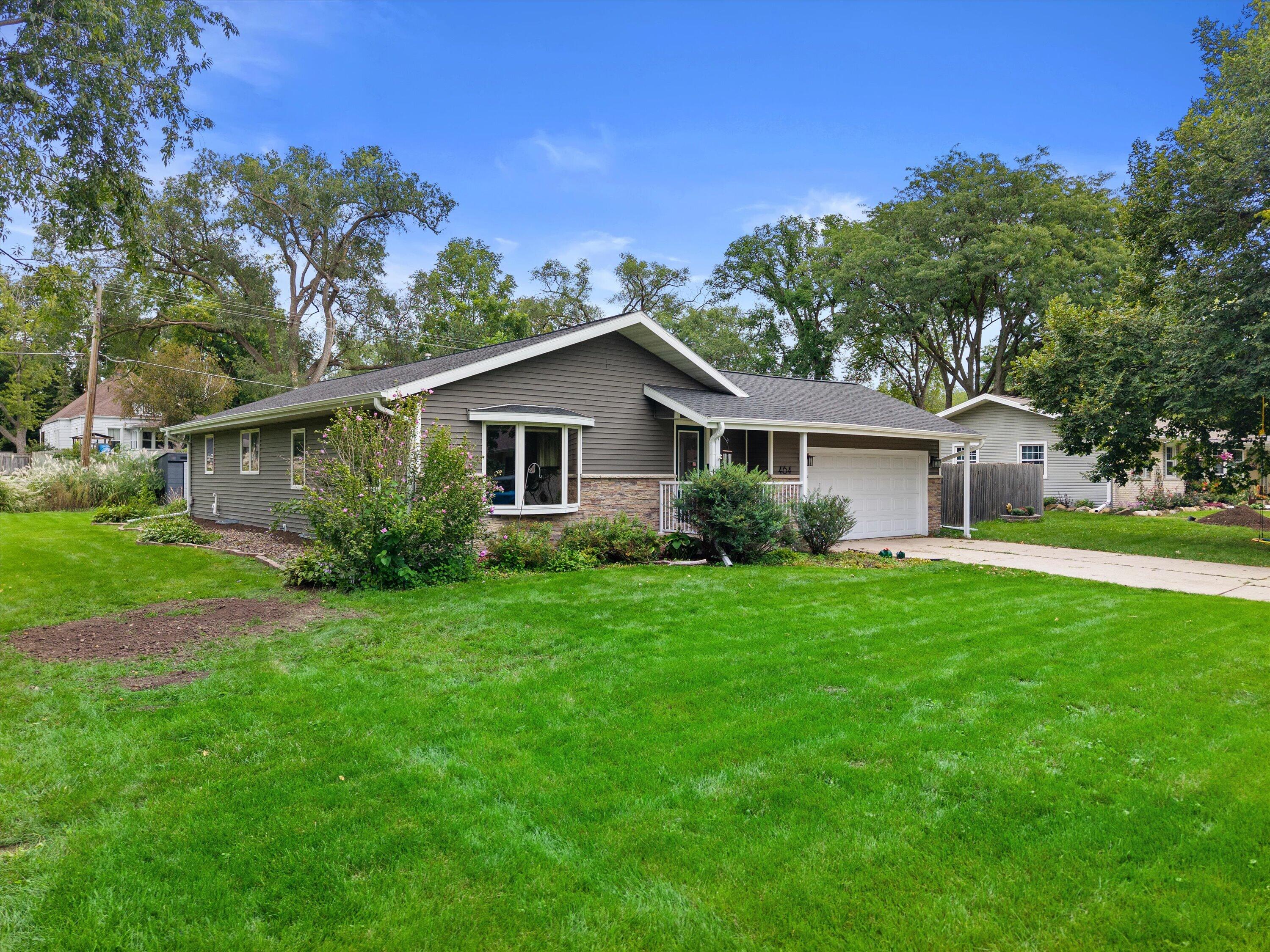 Single-story gray home with stone accents, white garage, and a broad green lawn.