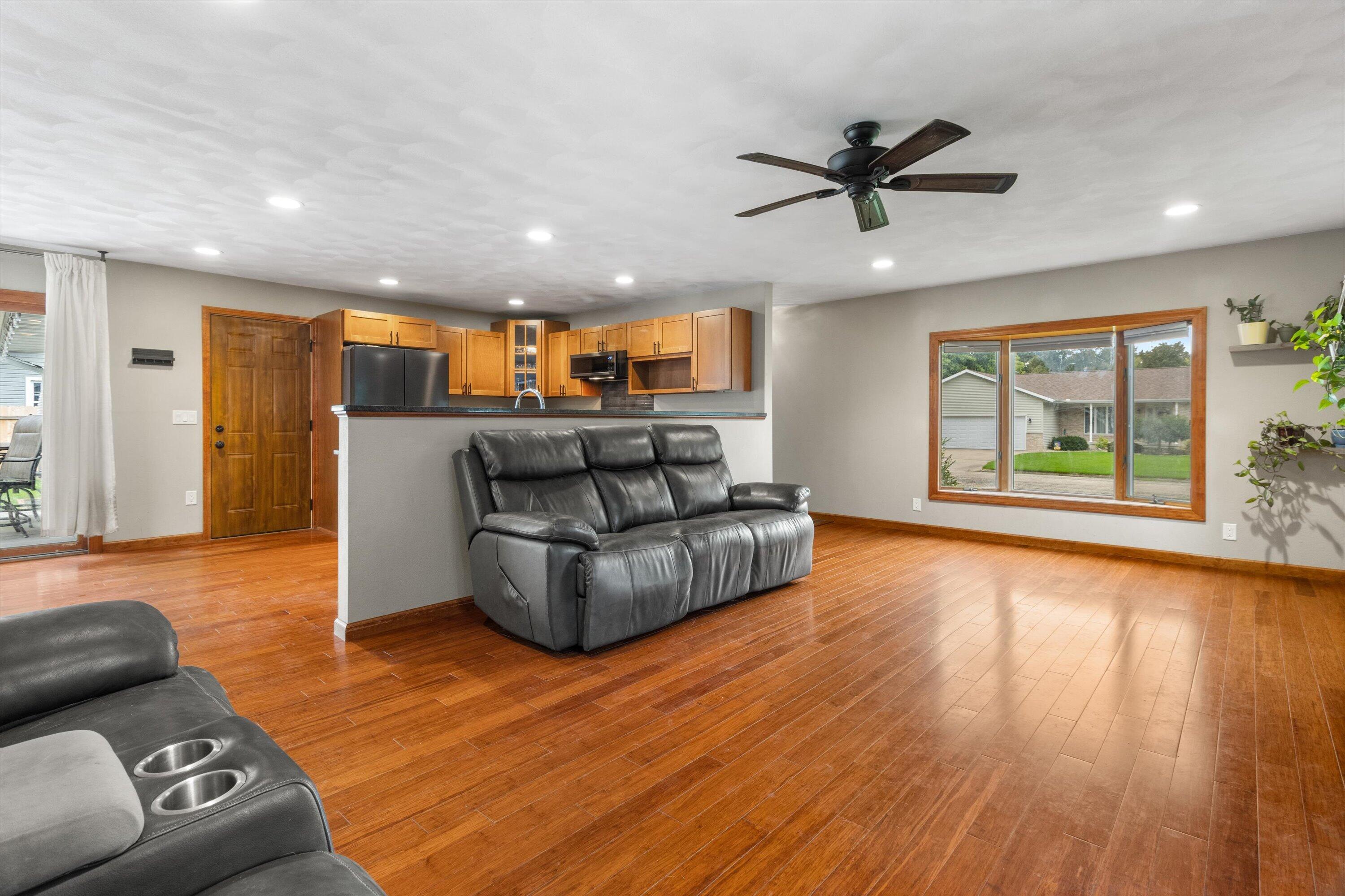 Living room with hardwood floors, leather reclining sofa, and open kitchen with wood cabinets.