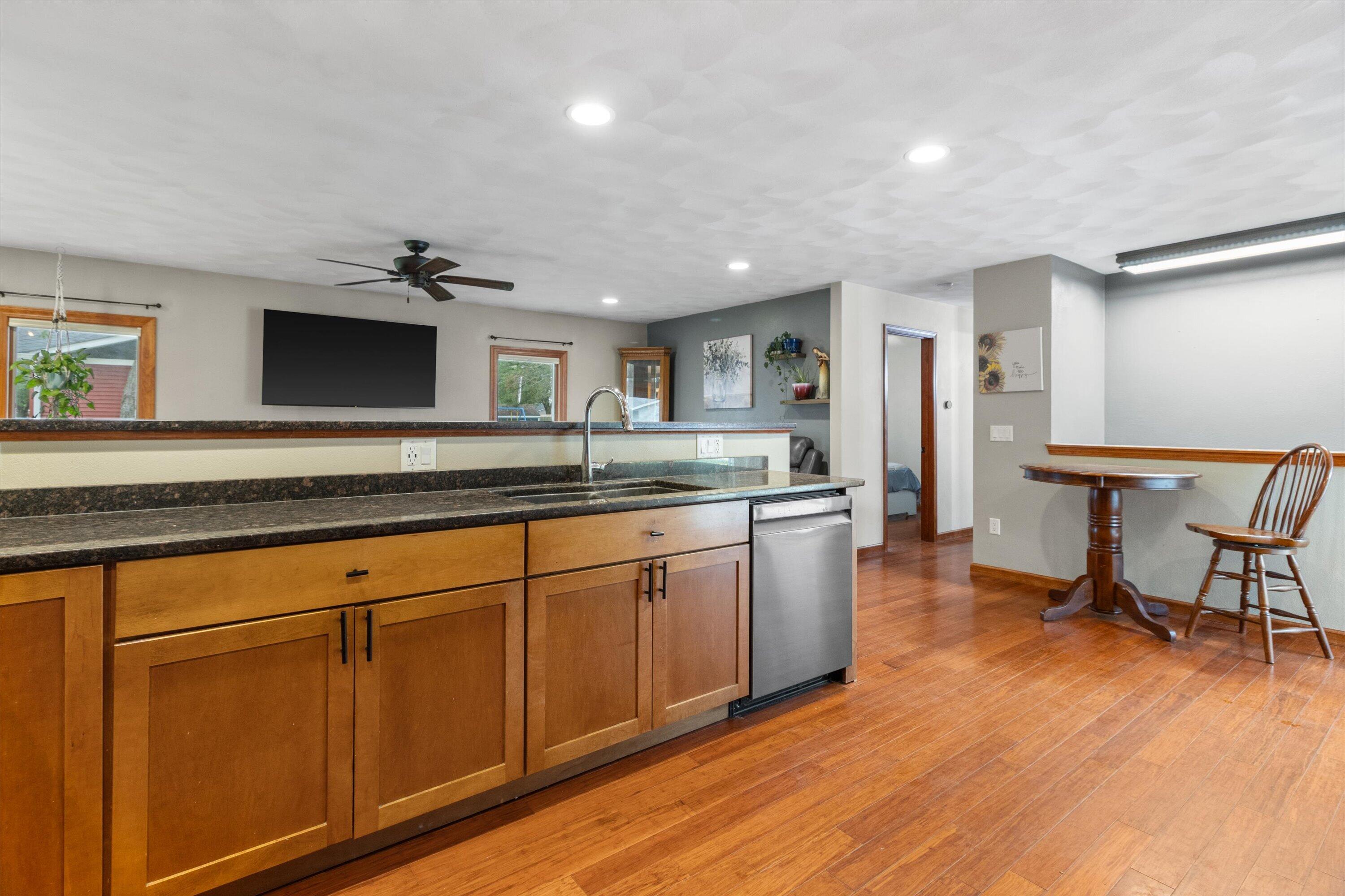 Kitchen with wood cabinets, dark counters, stainless steel dishwasher, and hardwood floors.