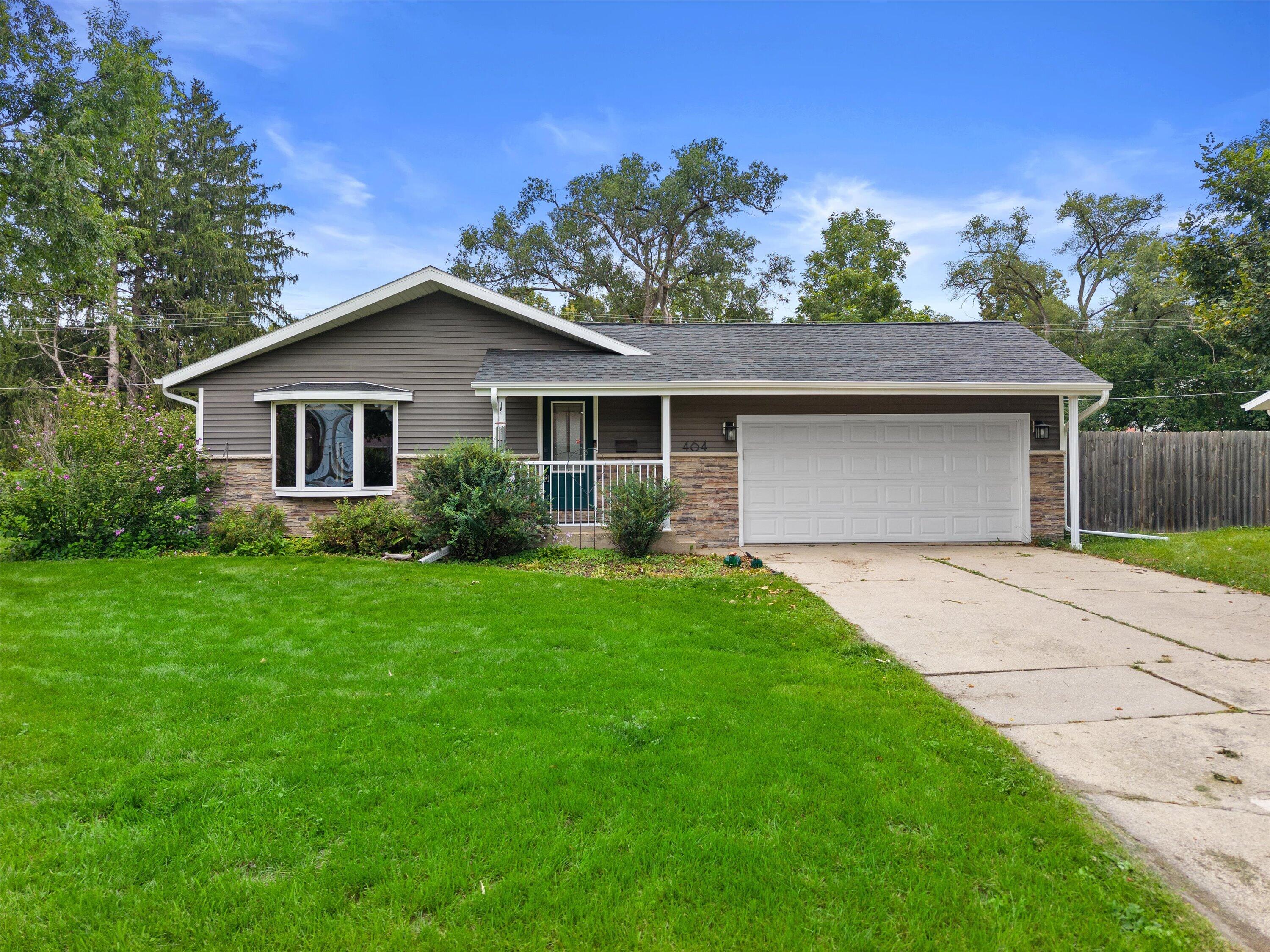 Single-story gray house with stone veneer, a two-car garage, bay window, and broad green lawn.