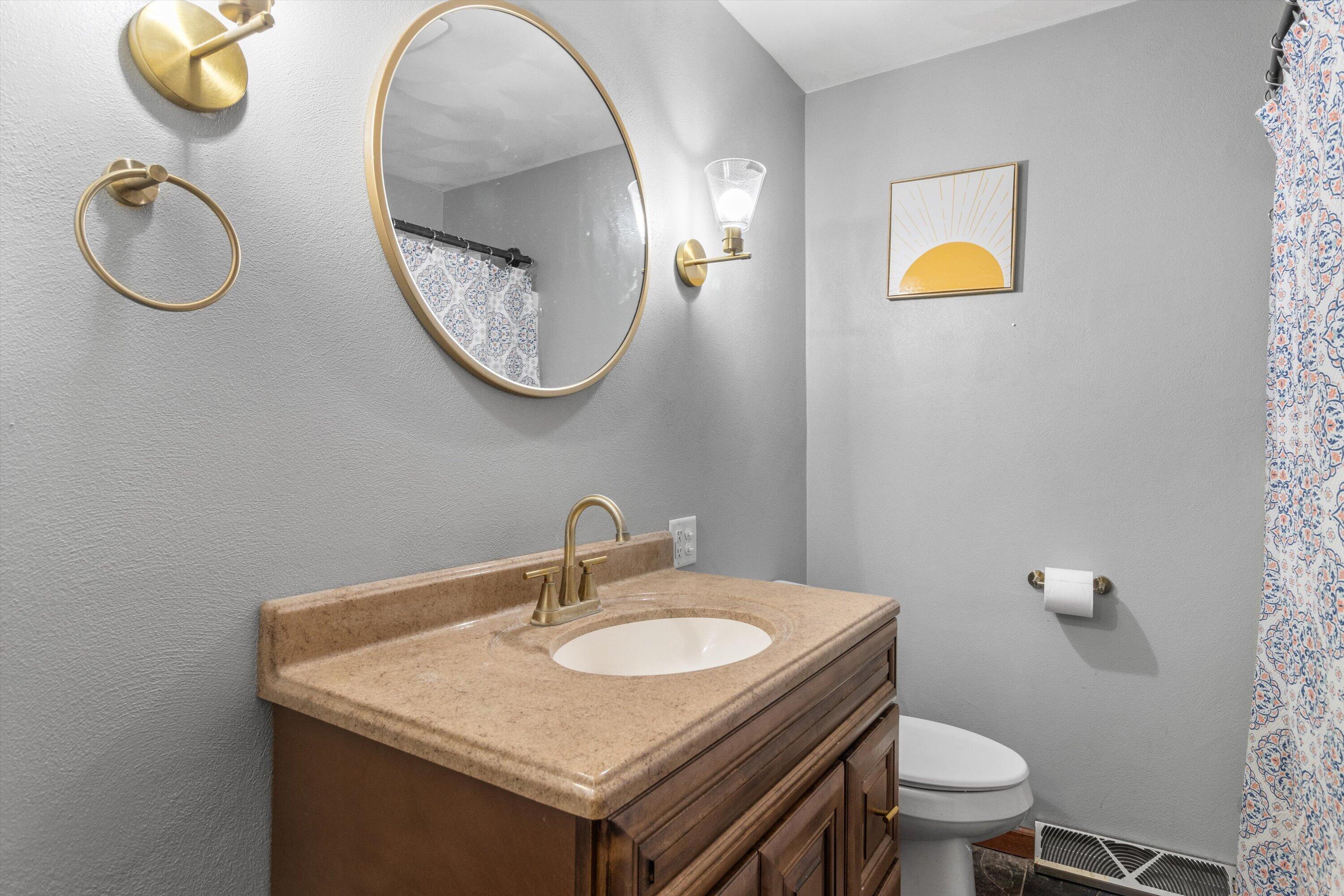 Bathroom with a dark wood vanity, brass fixtures, oval mirror, and patterned shower curtain.