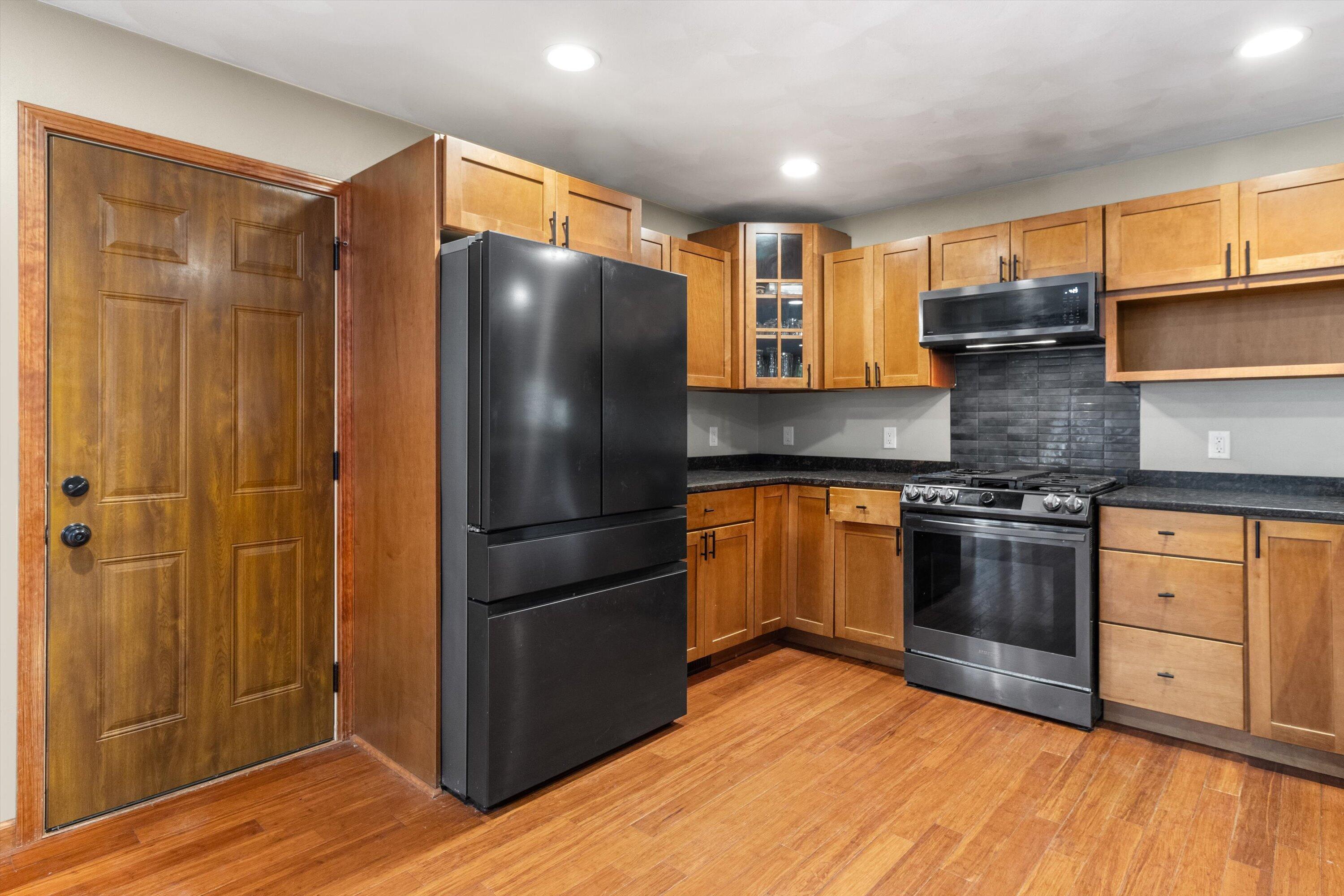 Kitchen with honey-toned wood cabinets, hardwood floors, and black and stainless steel appliances.