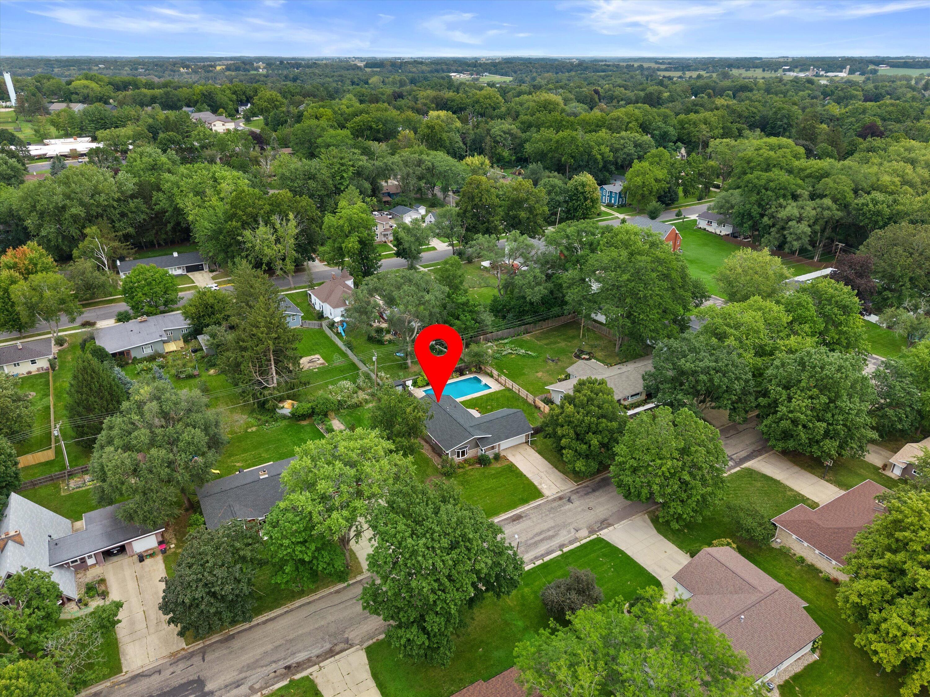 Aerial view of a gray-roofed home and backyard pool, marked by a red location pin among leafy homes.