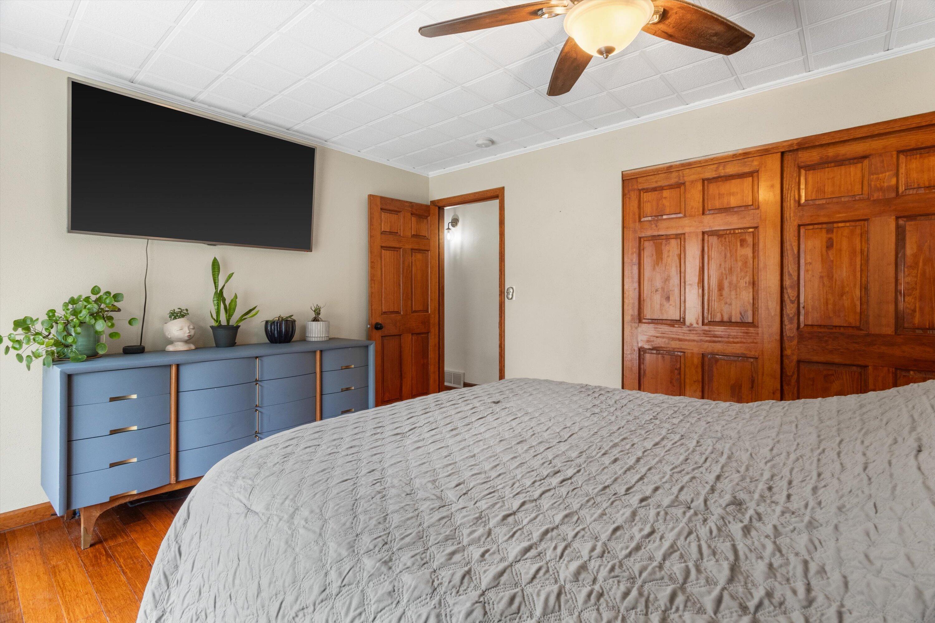 Bedroom with warm wood-paneled closet doors, a blue dresser, and a large gray-covered bed.