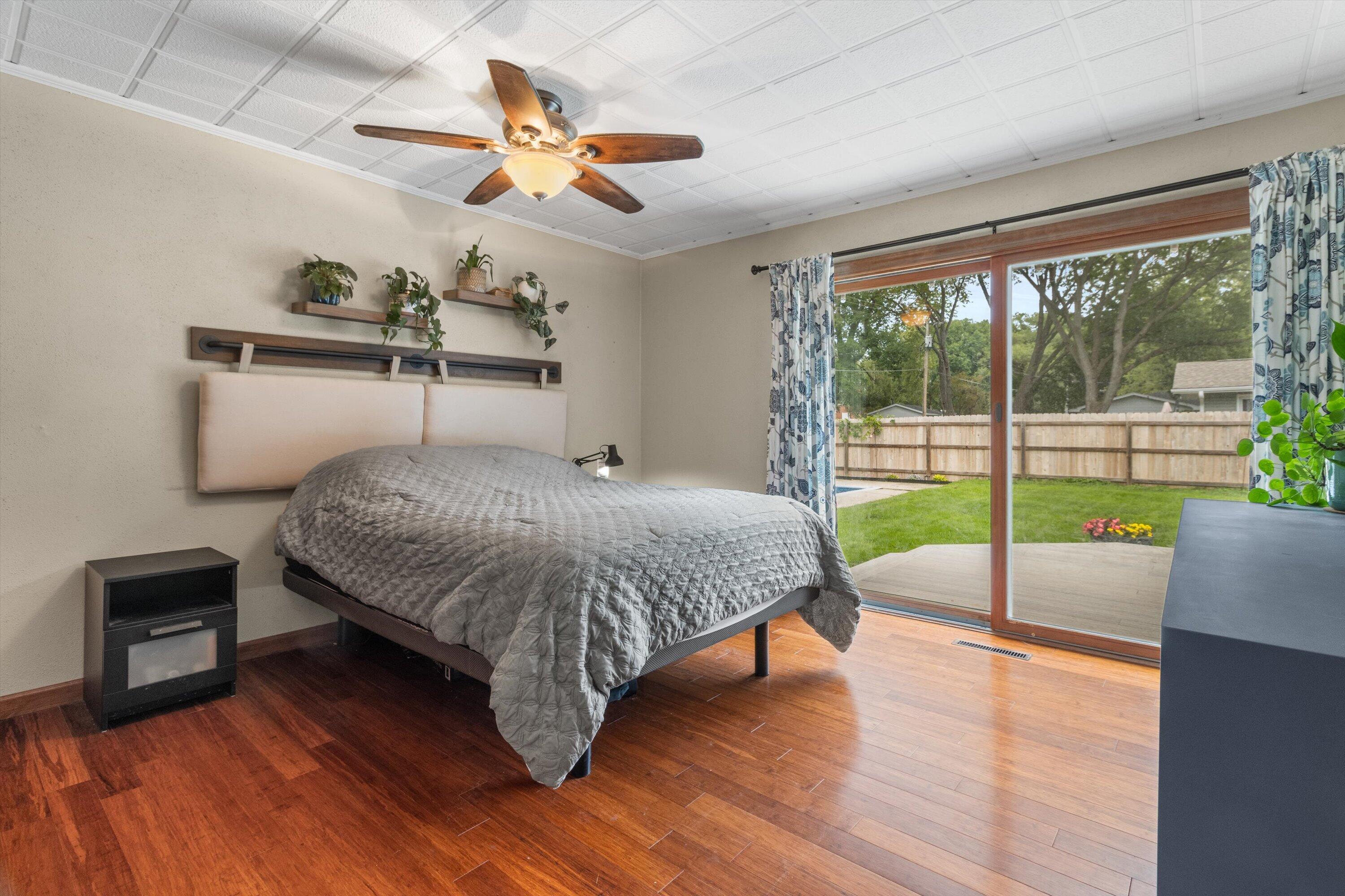 Bedroom with a gray quilted bed and sliding glass doors opening to a fenced backyard.