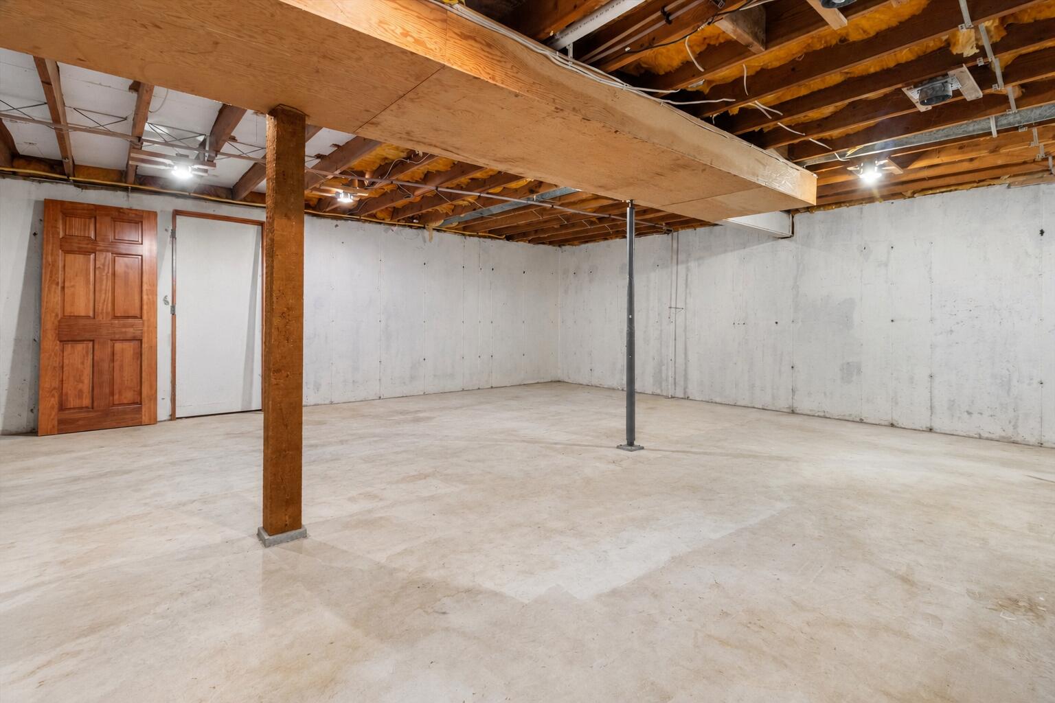 Unfinished basement with a concrete floor, exposed ceiling joists, and support posts.
