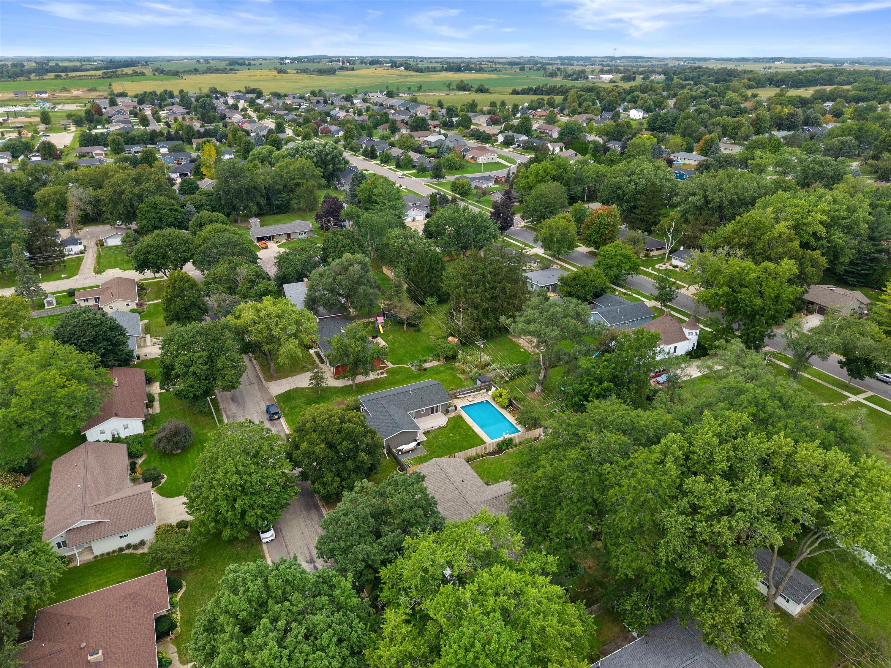 Aerial view of a leafy neighborhood with detached homes, intersecting streets, and a backyard swimming pool.