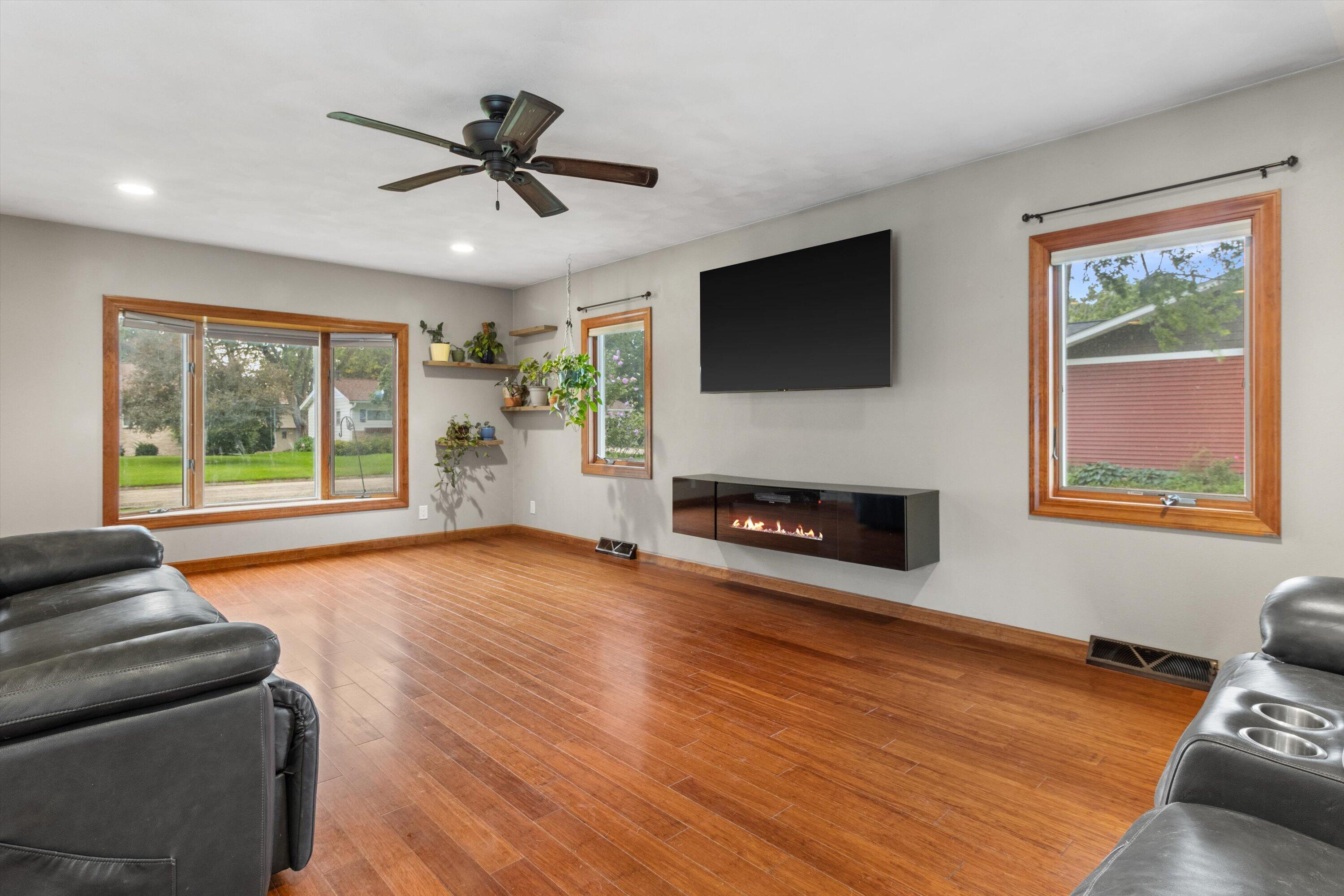 Living room with wood floors, black leather recliners, floating fireplace, and wall-mounted television.