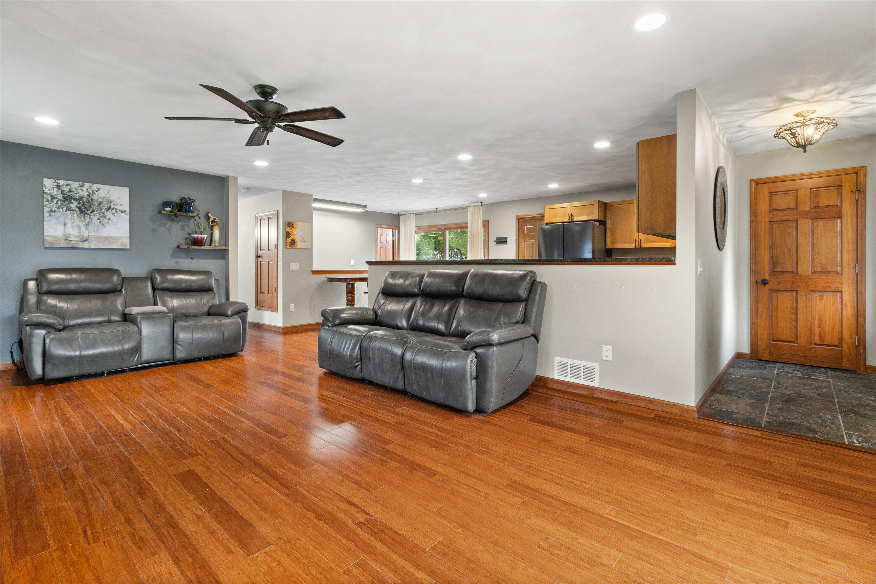 Open-plan living room with gray leather sofas, hardwood floors, and a view into the kitchen.