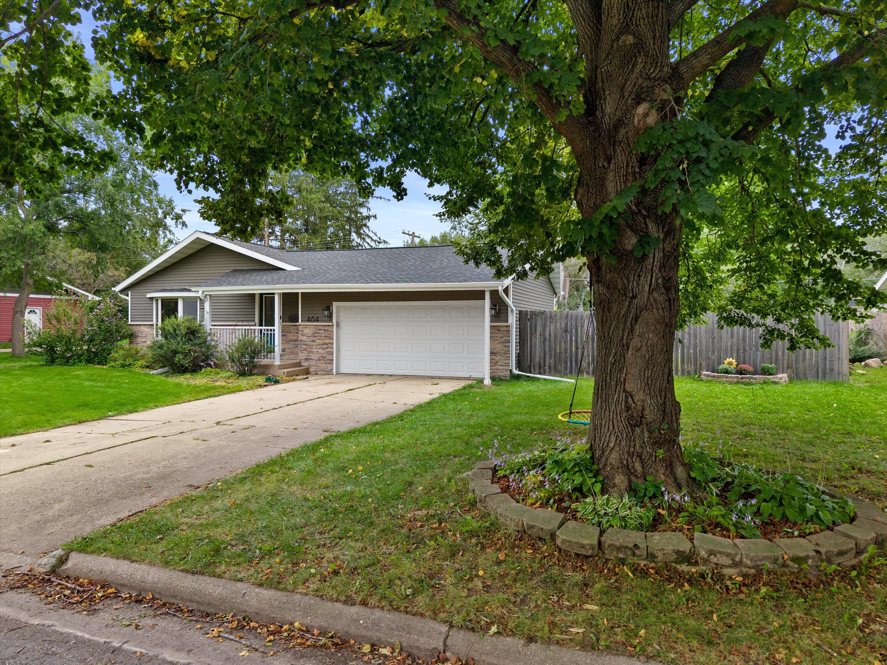 Single-story gray home with stone veneer, two-car garage, and a large shade tree in the front yard.