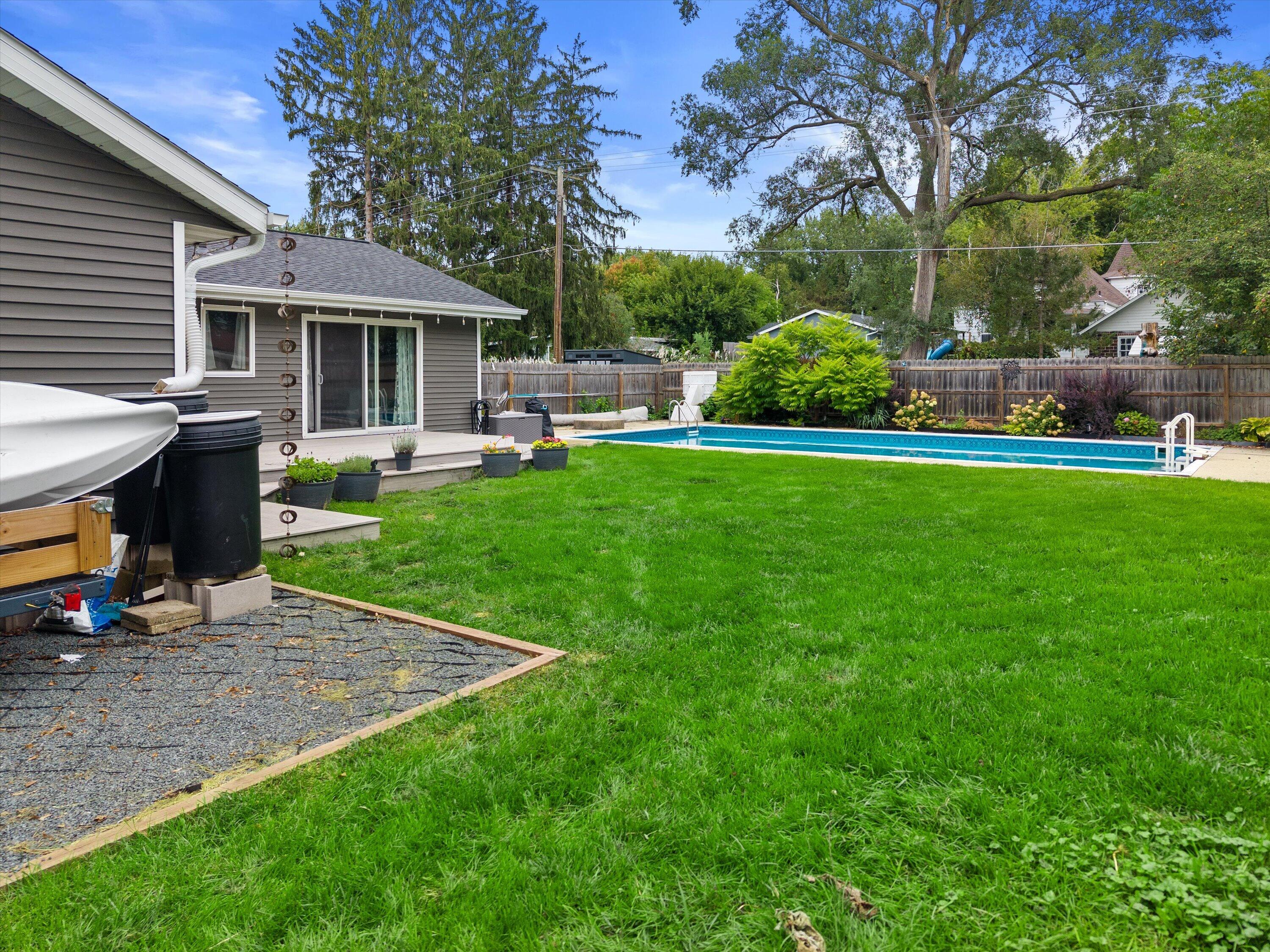 Fenced backyard with a long swimming pool, spacious lawn, and gray-sided house with a deck.
